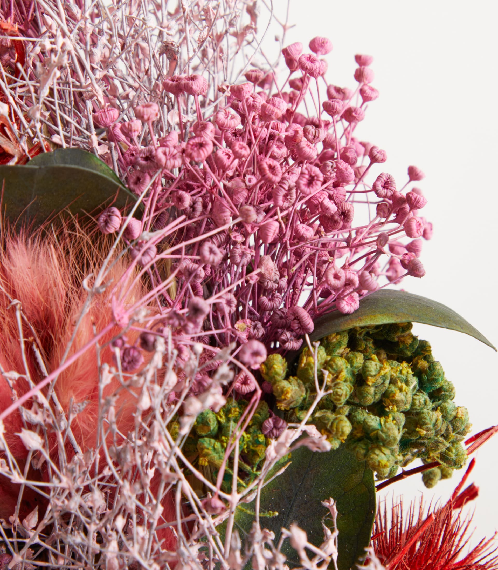 Ein lebendiger Strauß verschiedener Blumen, darunter eine auffällige rote Proteablüte, umgeben von üppigem Grün und zarten violetten Akzenten, wodurch ein optisch ansprechendes und strukturiertes Arrangement entsteht.