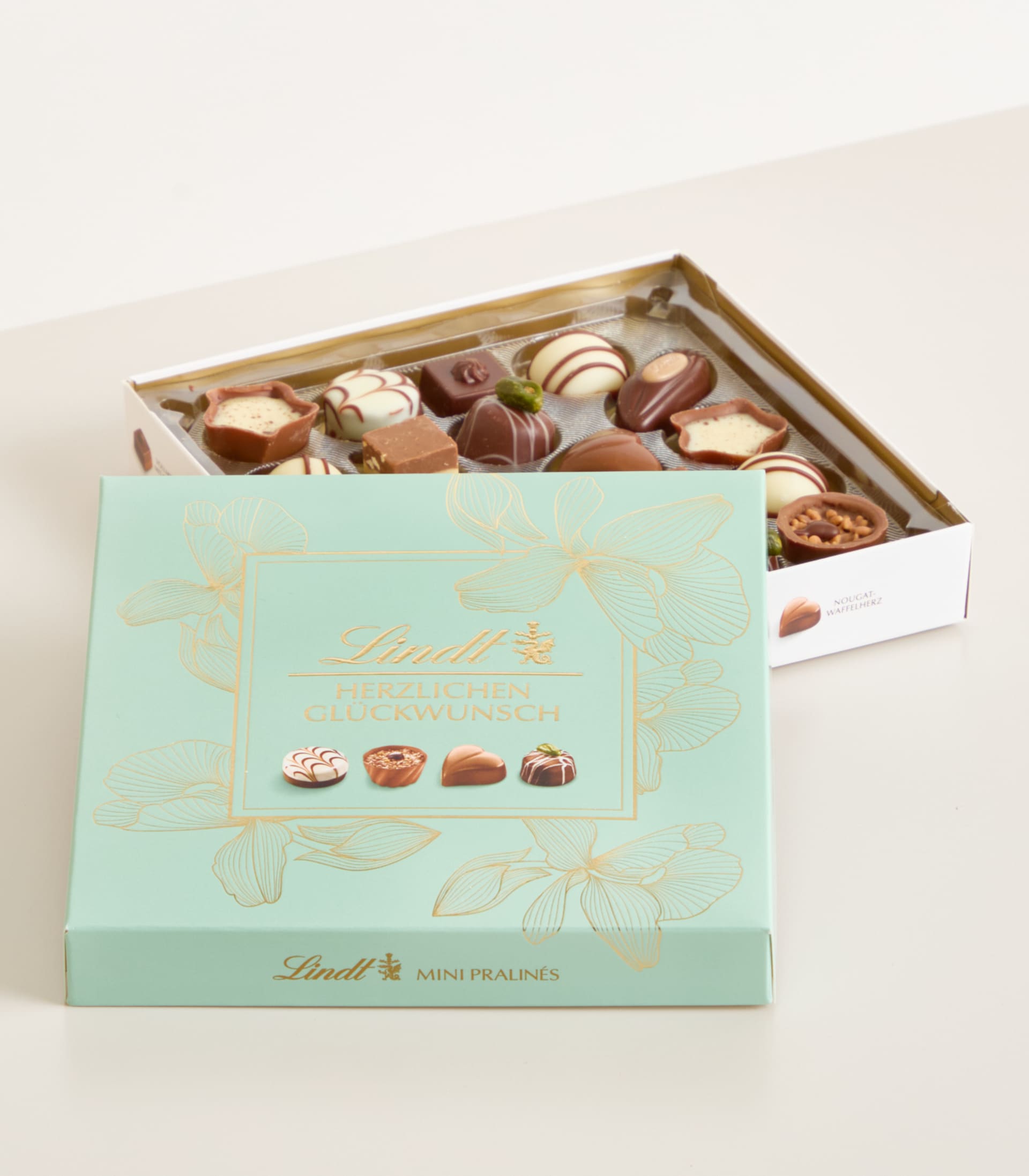 Eine Schachtel mit verschiedenen Lindt-Schokoladen in einer mintgrünen und goldenen Verpackung, die auf einer hellen Oberfläche liegt.