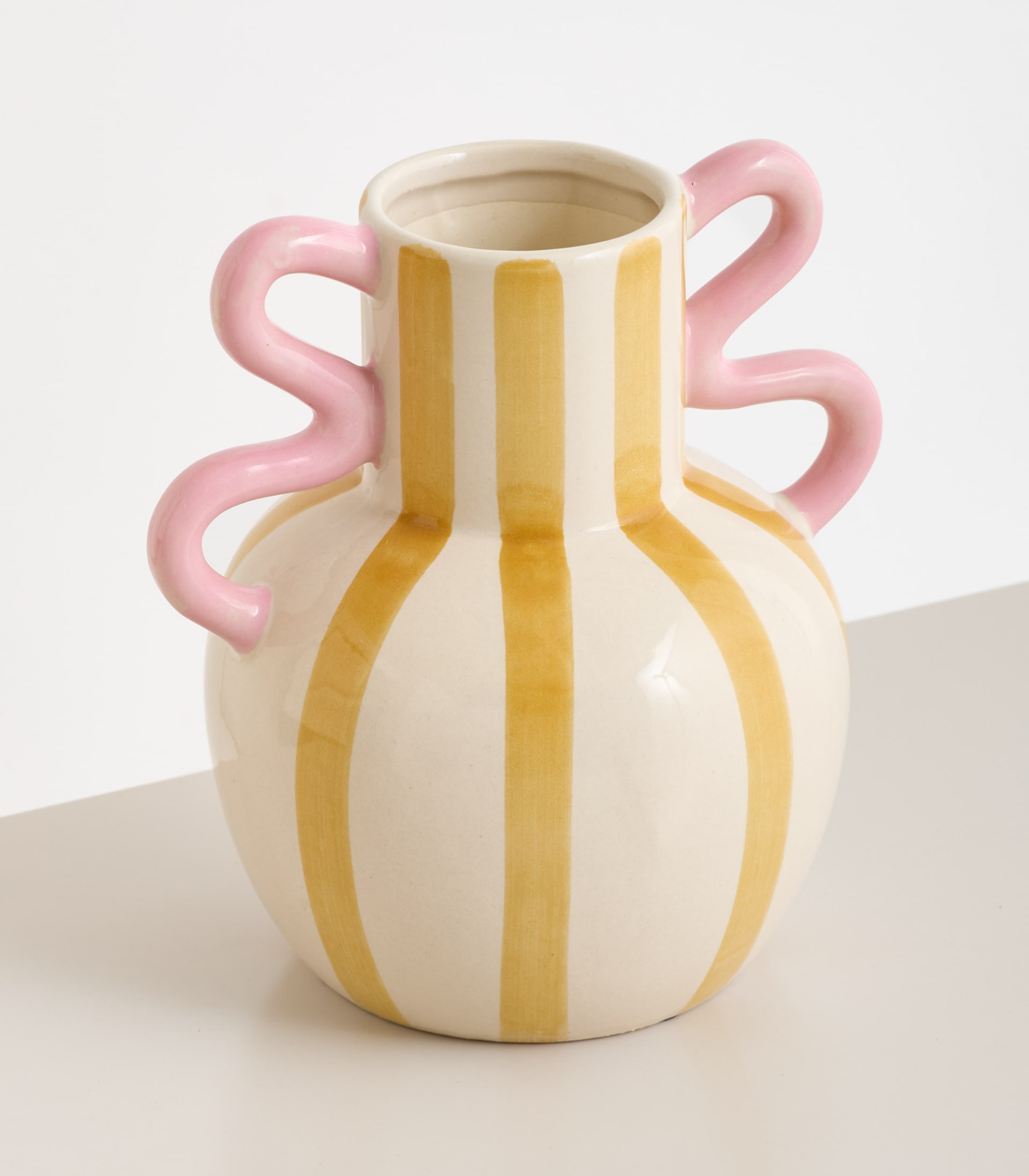 Eine Keramikvase mit einem einzigartigen, verspielten Design mit rosa Henkeln und gelben Streifen auf weißem Grund.