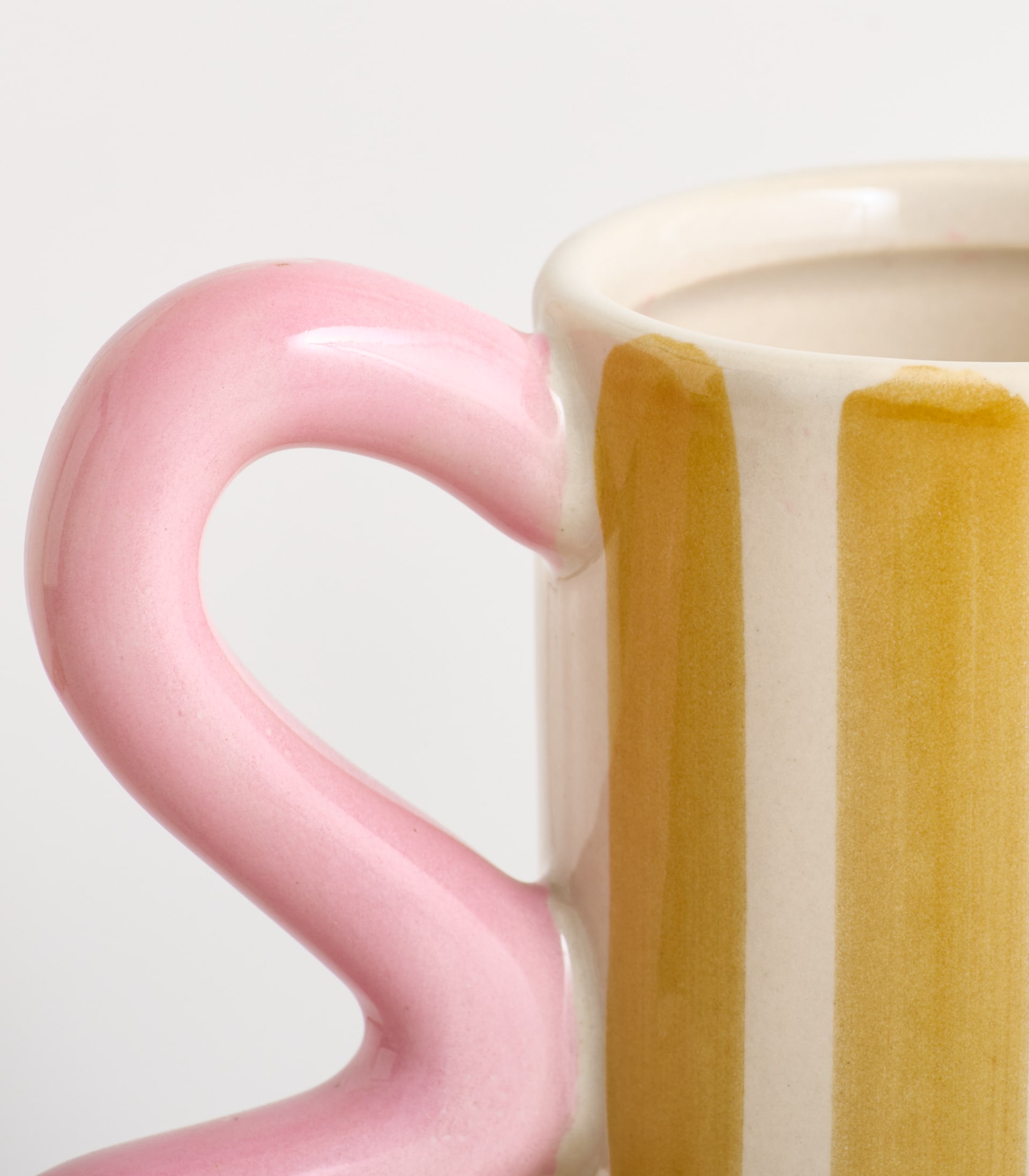 Eine rosa Keramiktasse mit gebogenem Henkel steht auf einem schlichten weißen Hintergrund.