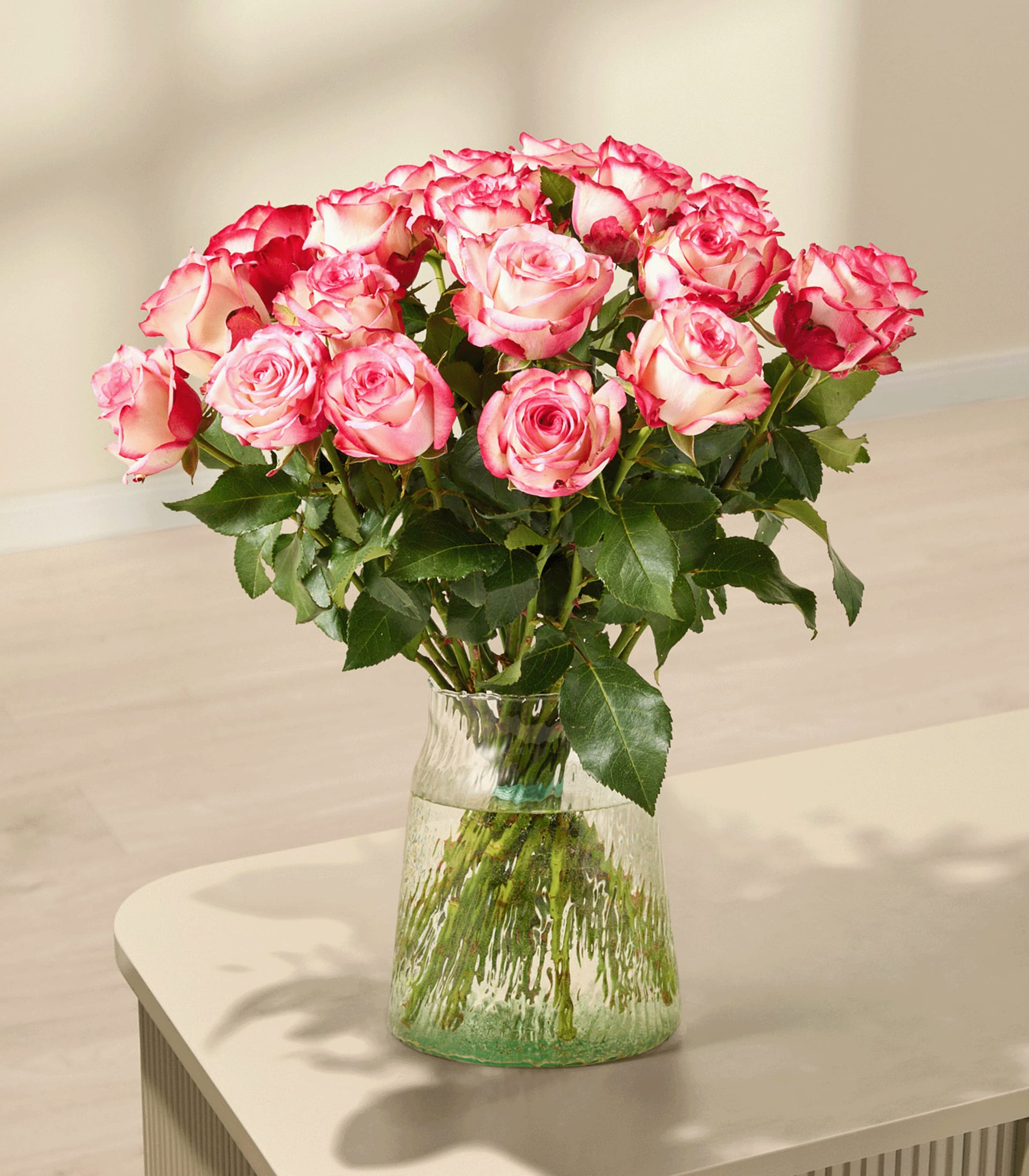 Ein Strauß leuchtend rosa Rosen, den eine Person vor einem schlichten weißen Hintergrund in den Händen hält.