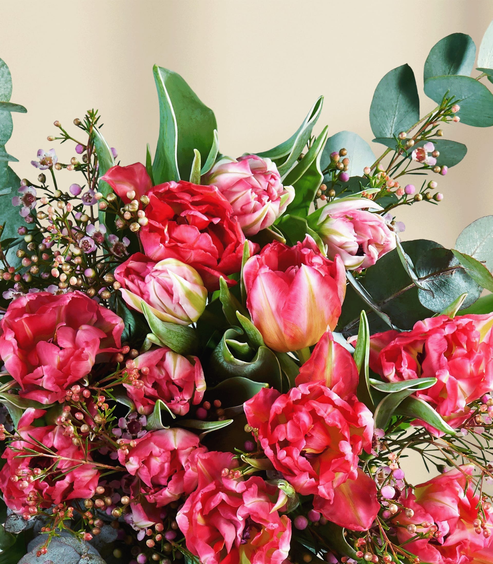 Ein leuchtender Strauß rosa und roter Blumen, darunter Tulpen, Pfingstrosen und andere Blüten, arrangiert vor einem schlichten weißen Hintergrund.
