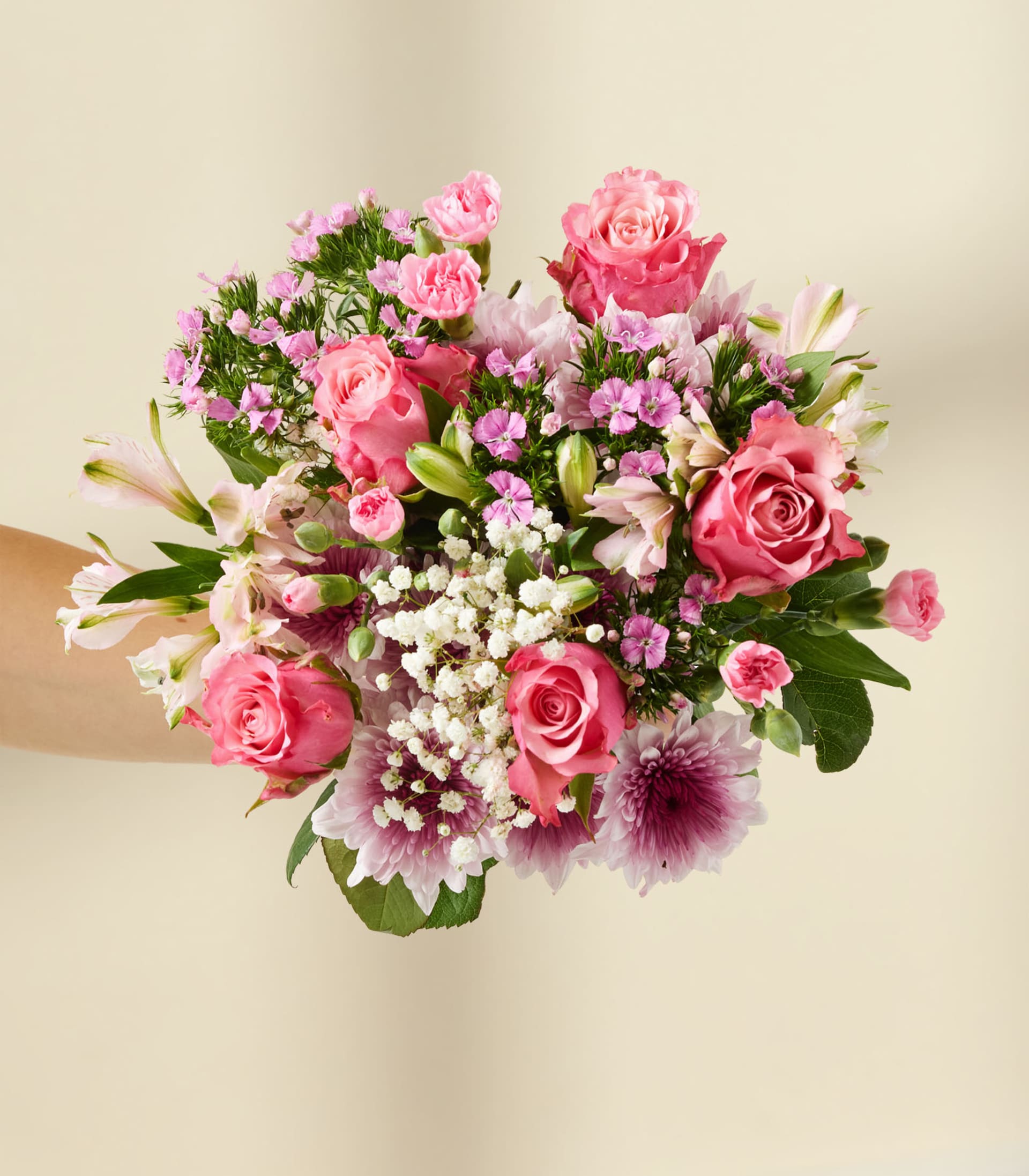 Eine junge Frau mit rotem Haar und einem floralen Haarschmuck hält einen leuchtend bunten Blumenstrauß vor einem schlichten weißen Hintergrund.