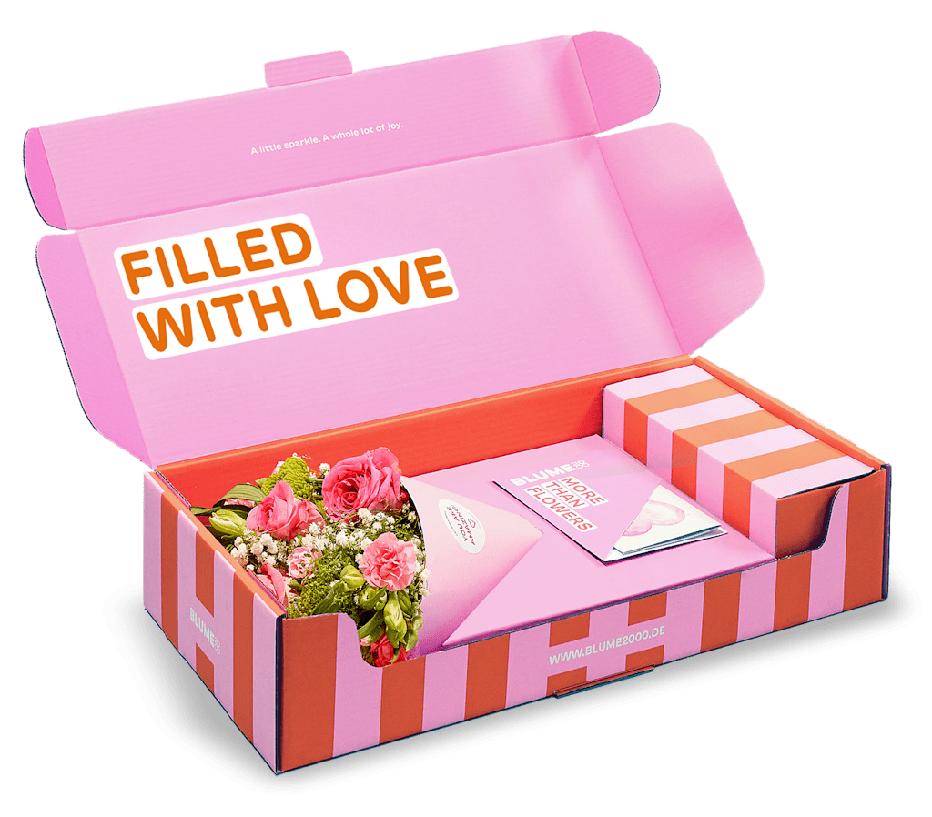 Eine rosa-orangefarbene Geschenkbox mit der Aufschrift „VOLL MIT LIEBE“ enthält einen Strauß bunter Blumen.
