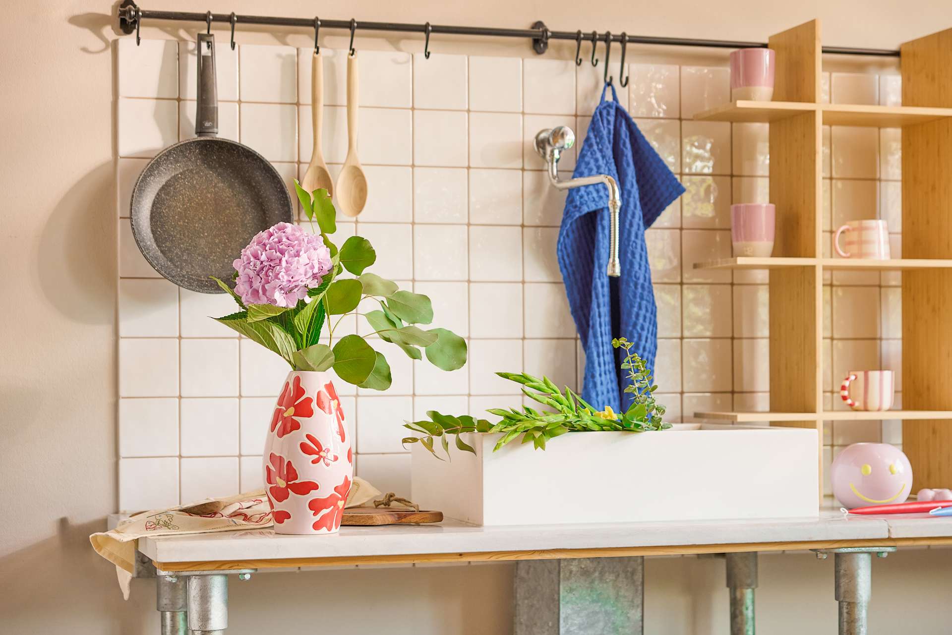 Eine gemütliche Kücheneinrichtung mit verschiedenen Kochutensilien, einer Vase mit rosa Blumen und Regalen mit Dekorationsartikeln.