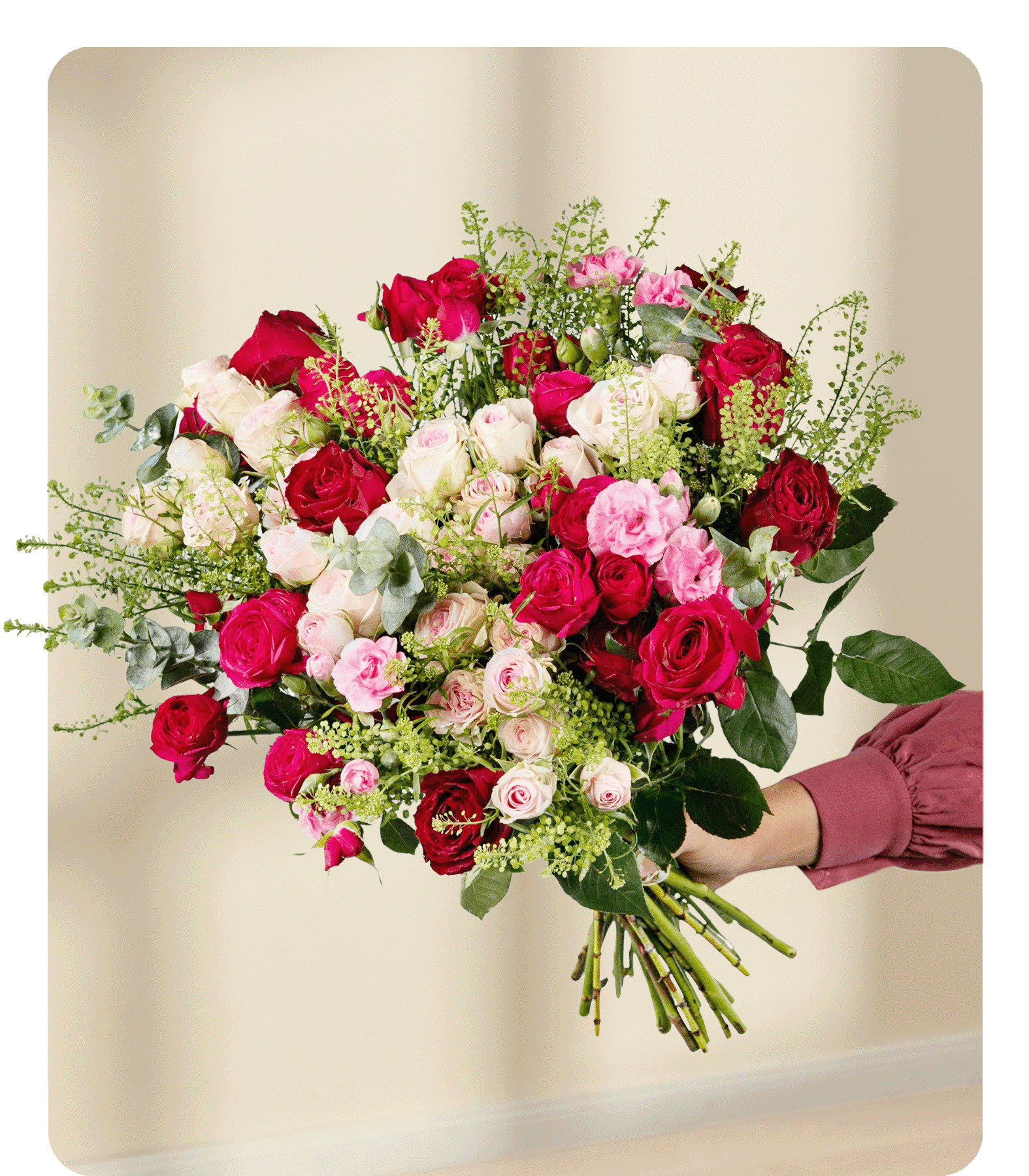 Ein großer, leuchtender Strauß aus roten und rosa Rosen, Nelken und anderen Blumen, den eine Person vor einem schlichten weißen Hintergrund in den Händen hält.