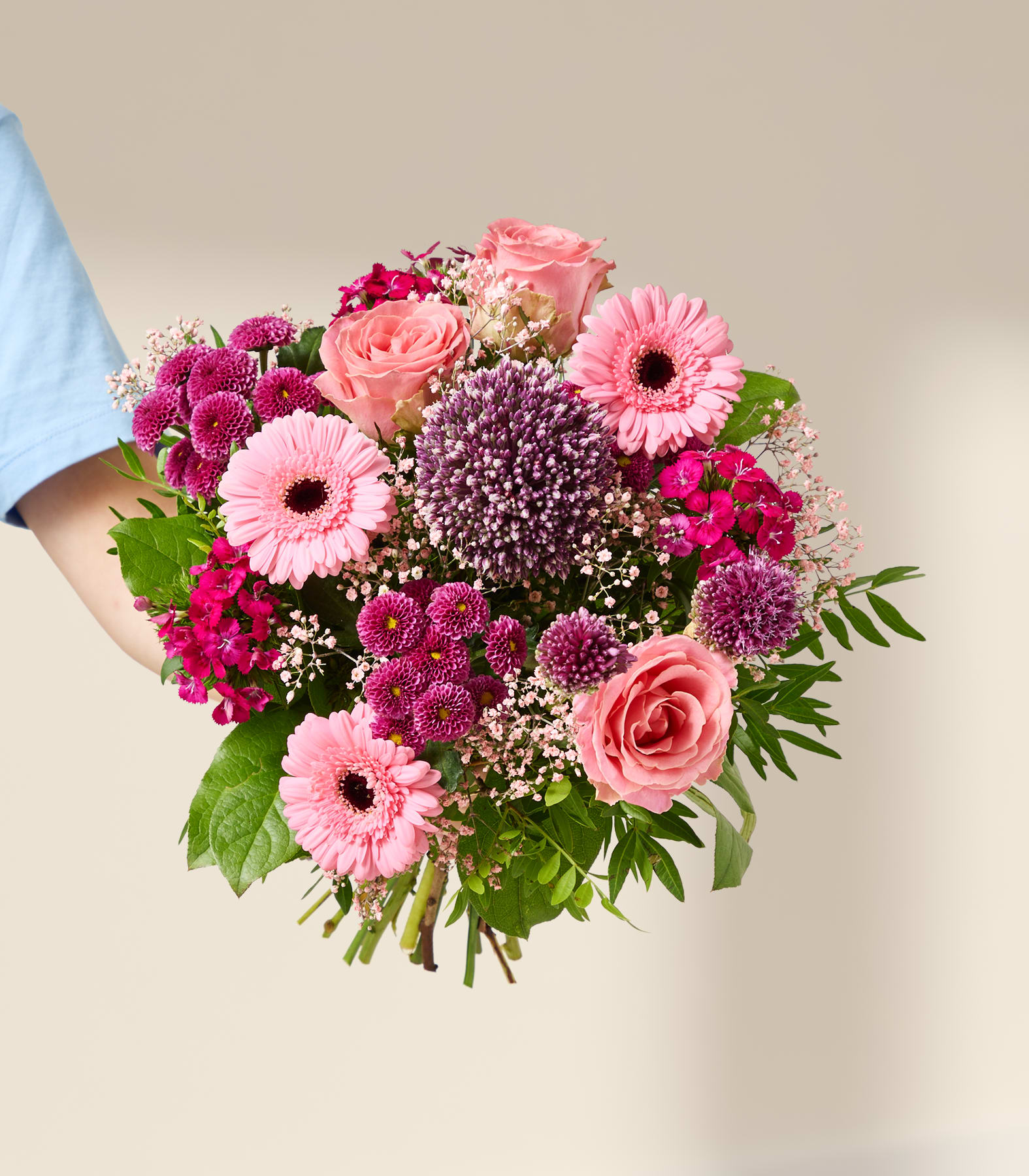 Im Vordergrund füllt ein leuchtender Strauß rosa und violetter Blumen eine Glasvase vor einem sanft beleuchteten, neutralen Hintergrund.