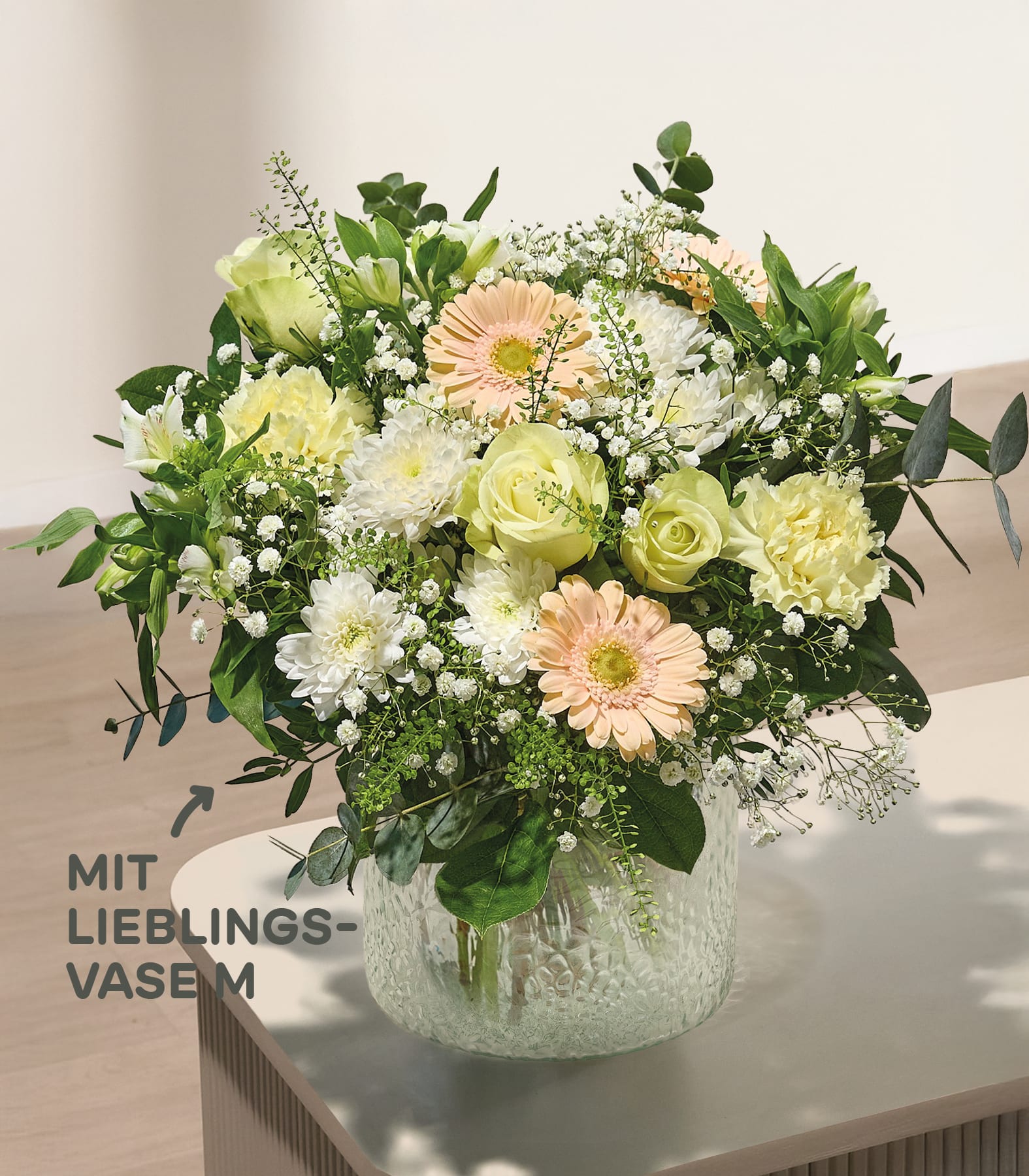 Im Vordergrund füllt ein leuchtender Strauß gelber und rosafarbener Blumen mit Schleierkraut eine strukturierte Glasvase vor einem weichen, verschwommenen Hintergrund.