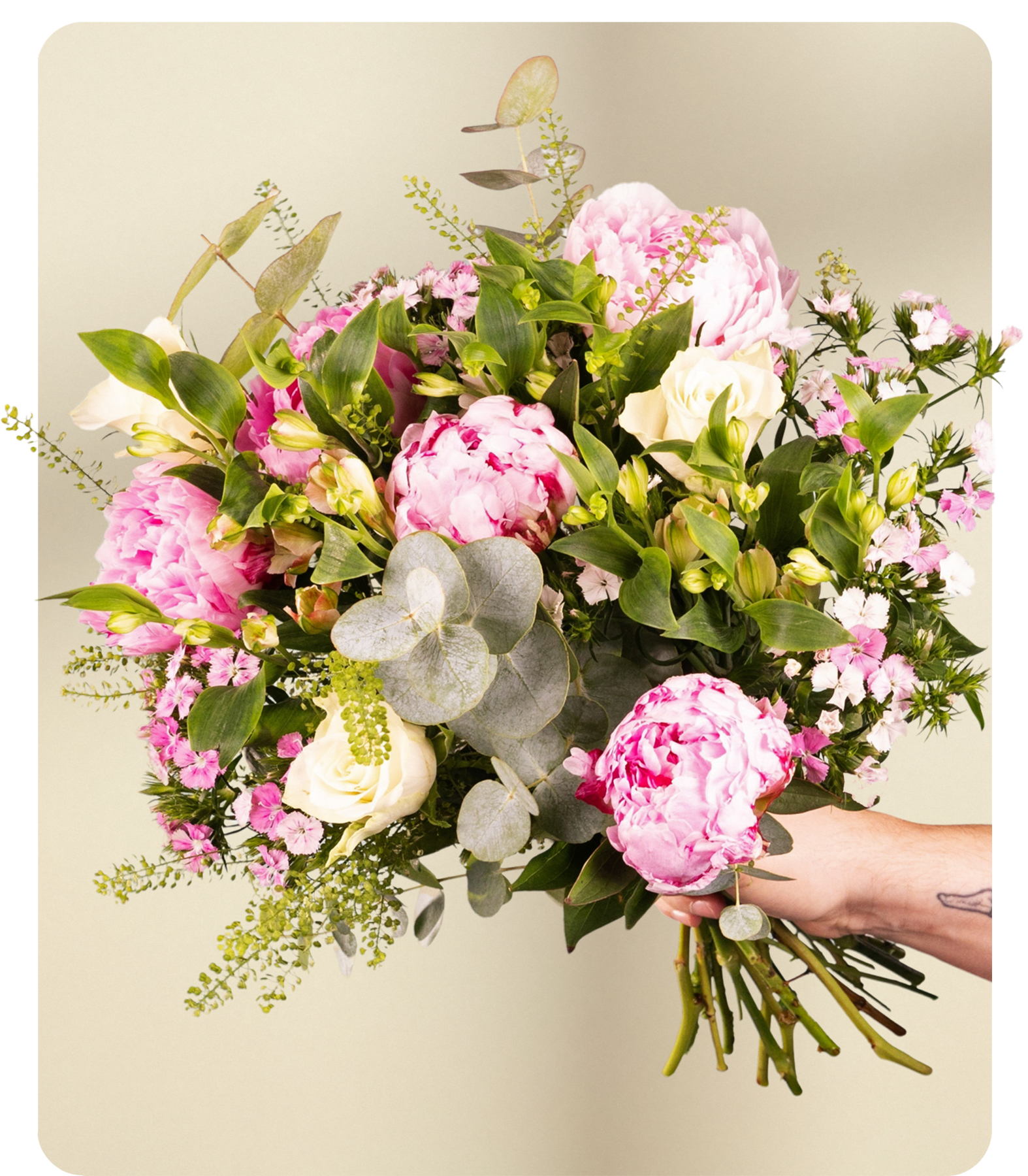 Eine Hand hält einen üppigen Strauß aus rosa Pfingstrosen, weißen Rosen und zarten rosa Wildblumen vor einem sanften, hellen Hintergrund.