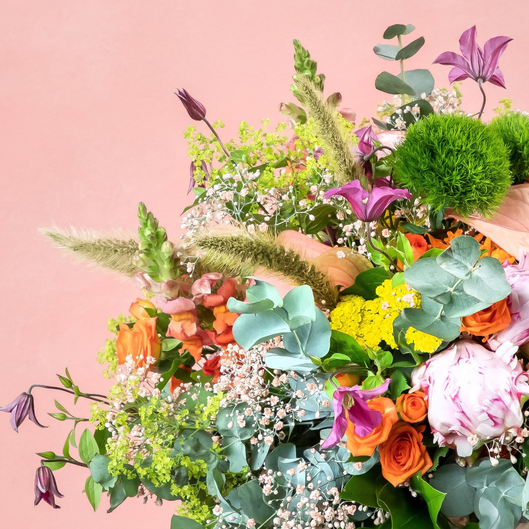 Ein lebendiger und üppiger Strauß verschiedener bunter Blumen, darunter Rosen, Lilien und Sukkulenten, vor einem zartrosa Hintergrund.