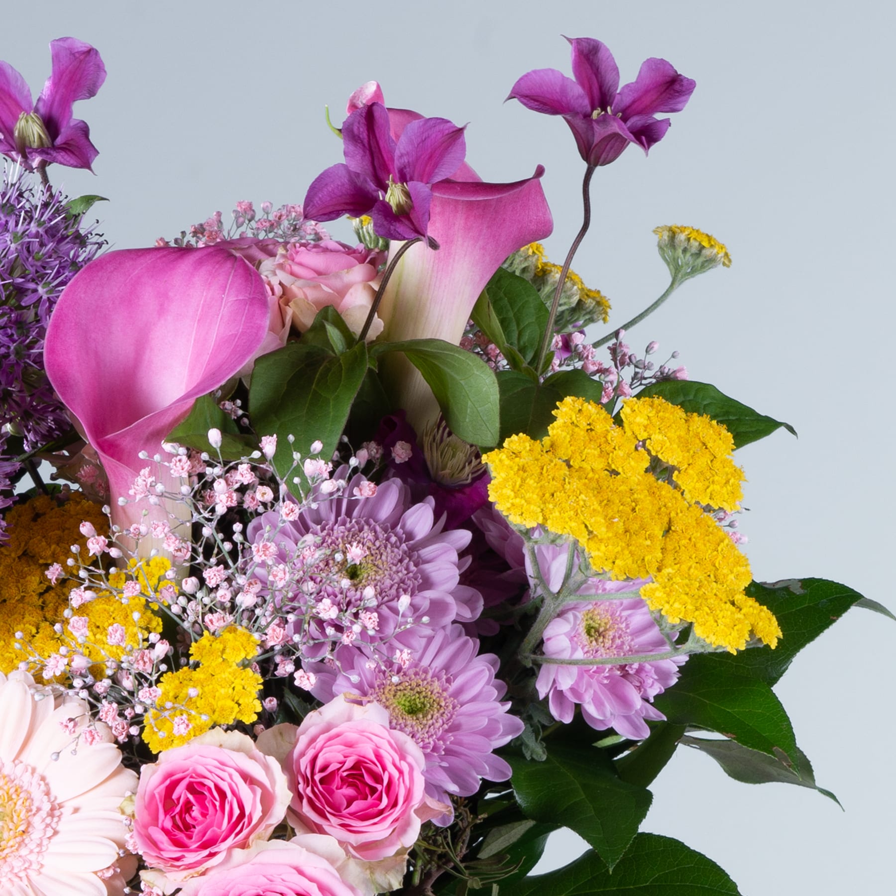 Ein lebendiger Strauß verschiedener bunter Blumen, darunter rosa Rosen, violette Orchideen und gelbe Chrysanthemen, vor einem hellblauen Hintergrund.