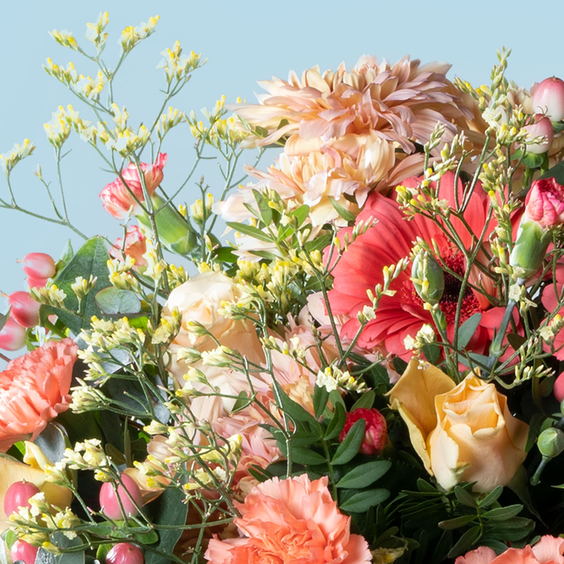 Ein lebendiger Strauß bunter Blumen, darunter rosa und gelbe Rosen, rote Nelken und gelbe Narzissen, vor einem sanften blauen Hintergrund.