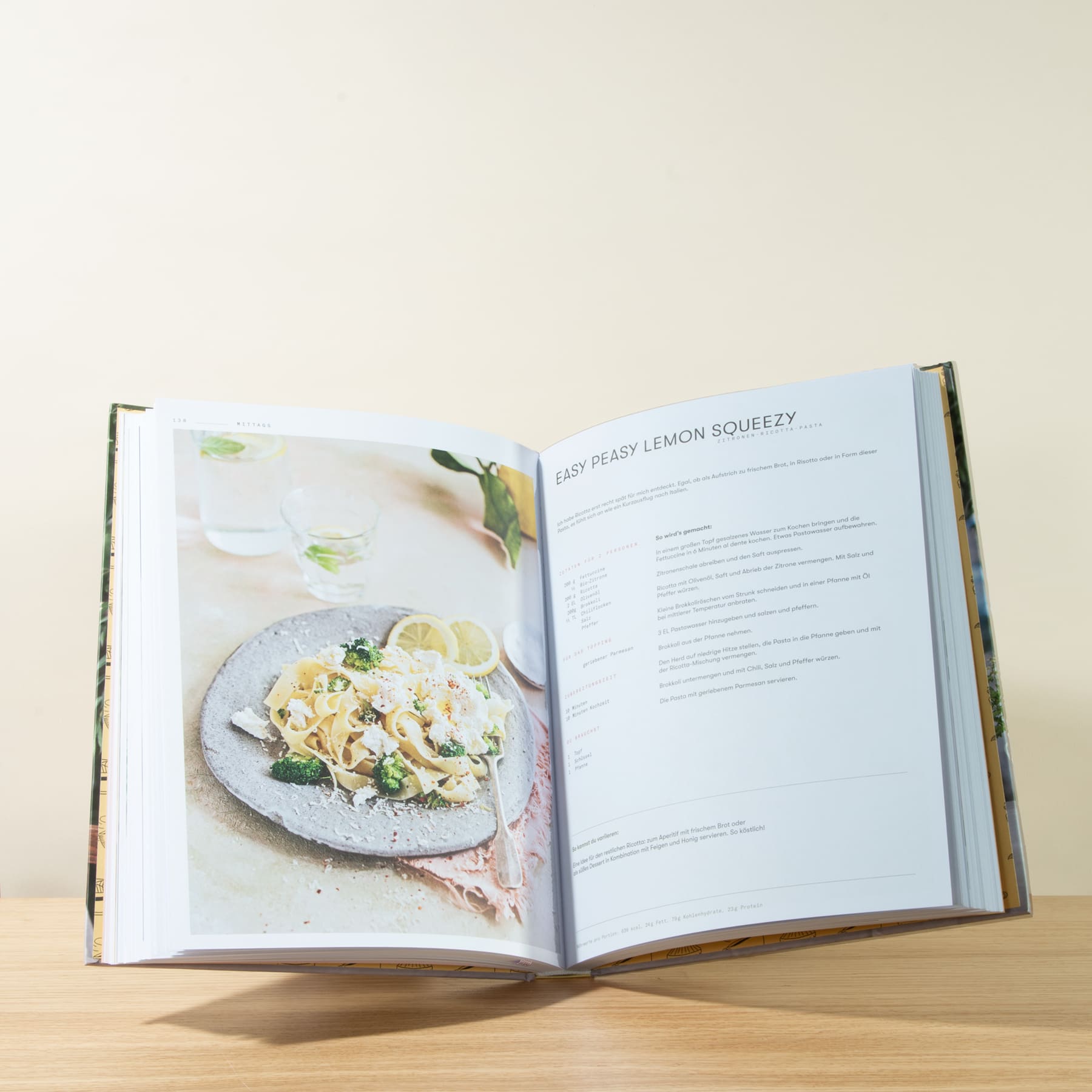 In einem aufgeschlagenen Kochbuch ist ein Rezept für ein Zitronengericht abgebildet, begleitet von einem Foto eines Tellers mit einem cremigen, mit Blumen garnierten Gericht.