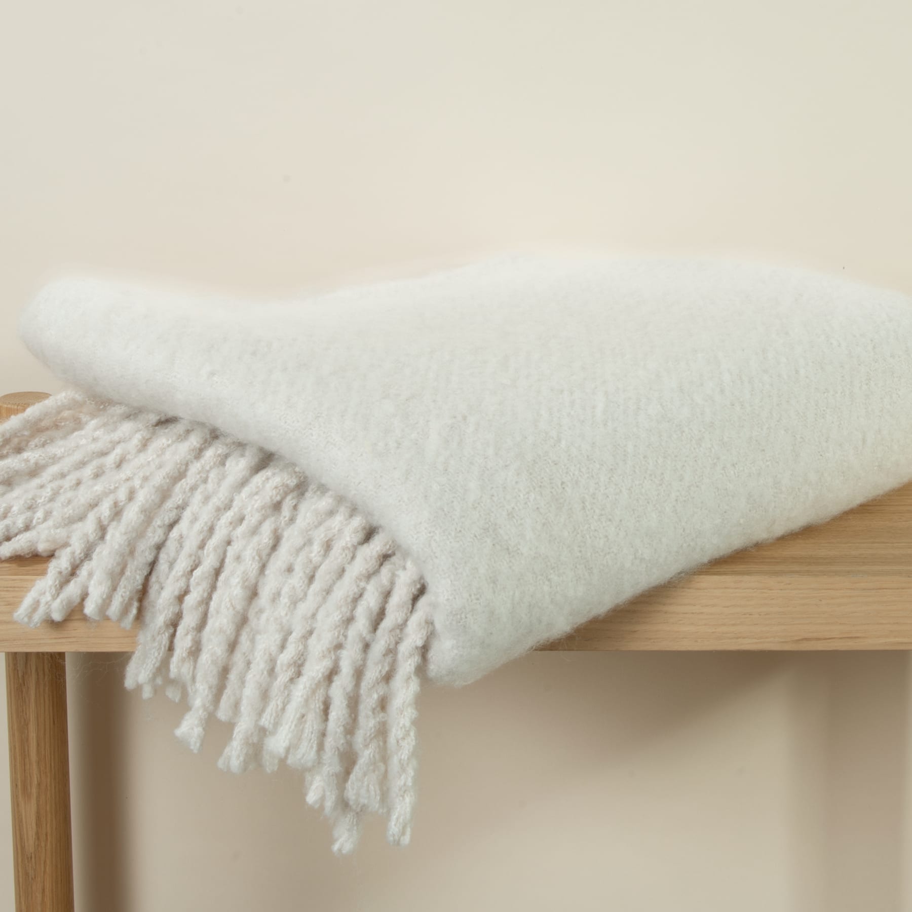 Eine gemütliche, weiße Strickdecke oder ein Überwurf wird über eine Holzbank oder ein Regal drapiert und schafft eine warme und einladende Atmosphäre.