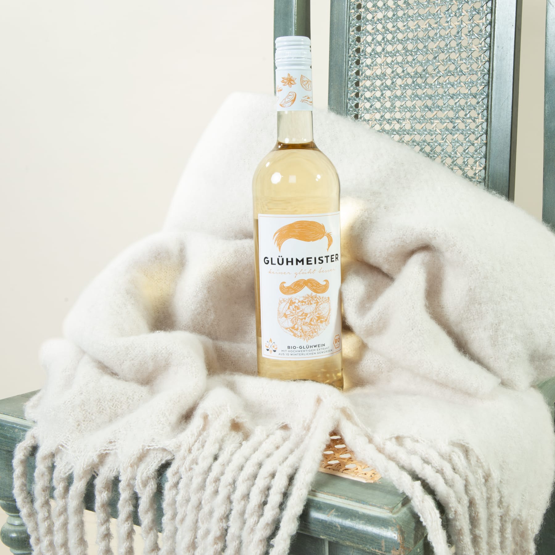 Eine Flasche Glühmeister steht auf einer weichen, flauschigen weißen Decke vor einem verspiegelten Hintergrund.
