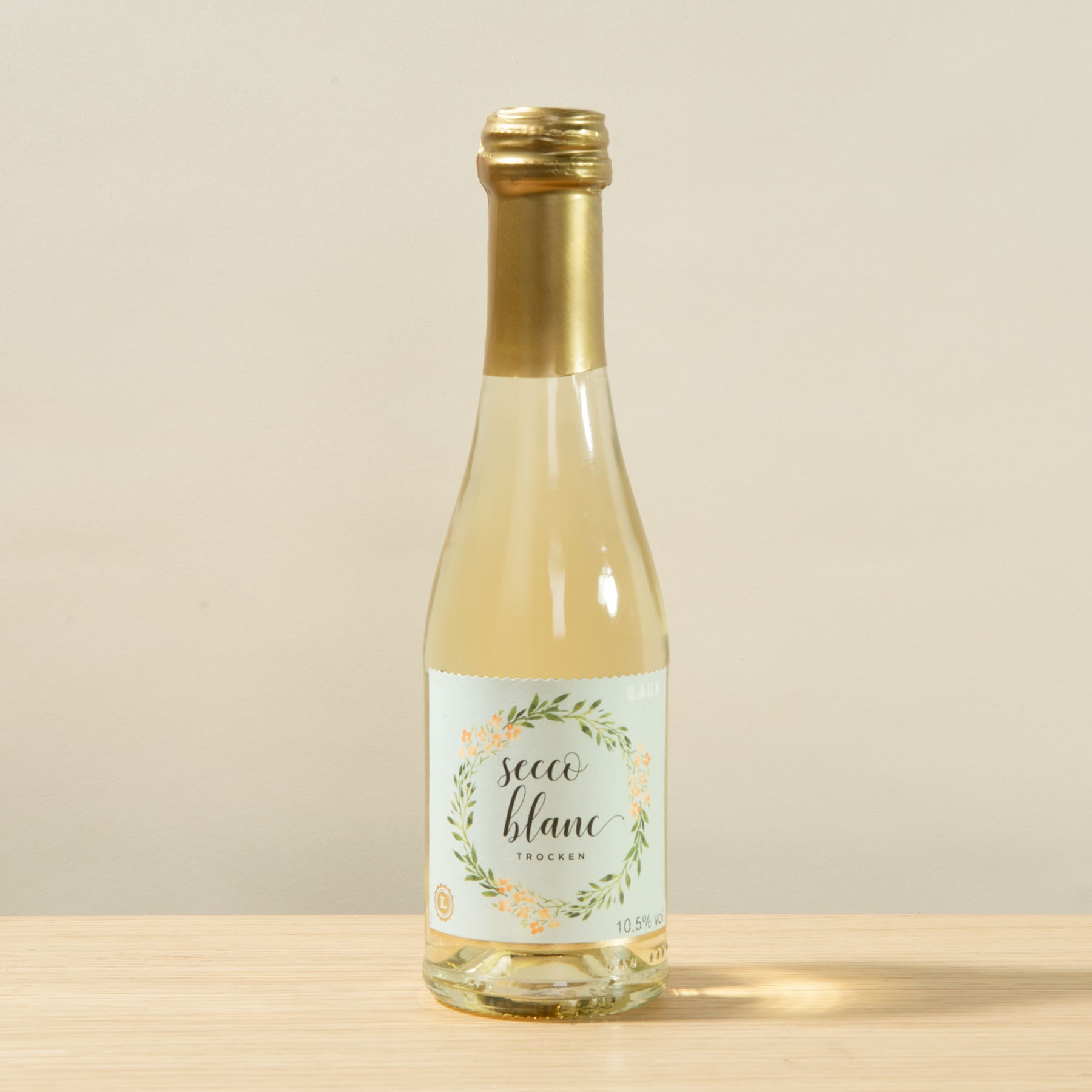 Eine Glasflasche mit goldenem Deckel, die eine helle Flüssigkeit enthält, steht auf einer Holzoberfläche vor einem schlichten beigen Hintergrund.