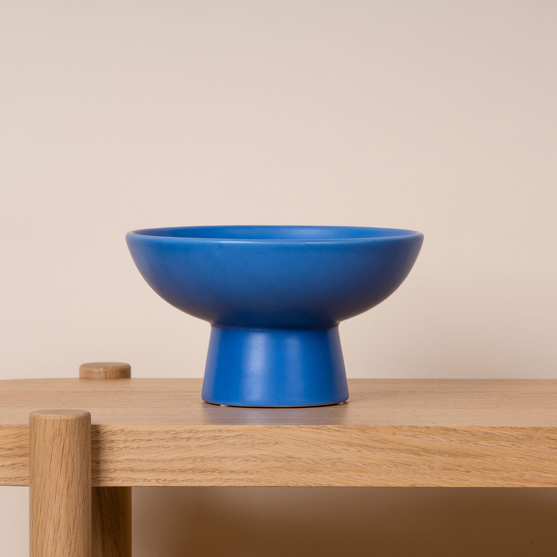 Eine blaue Keramikschale steht auf einem Holztisch vor einem neutralen Hintergrund.