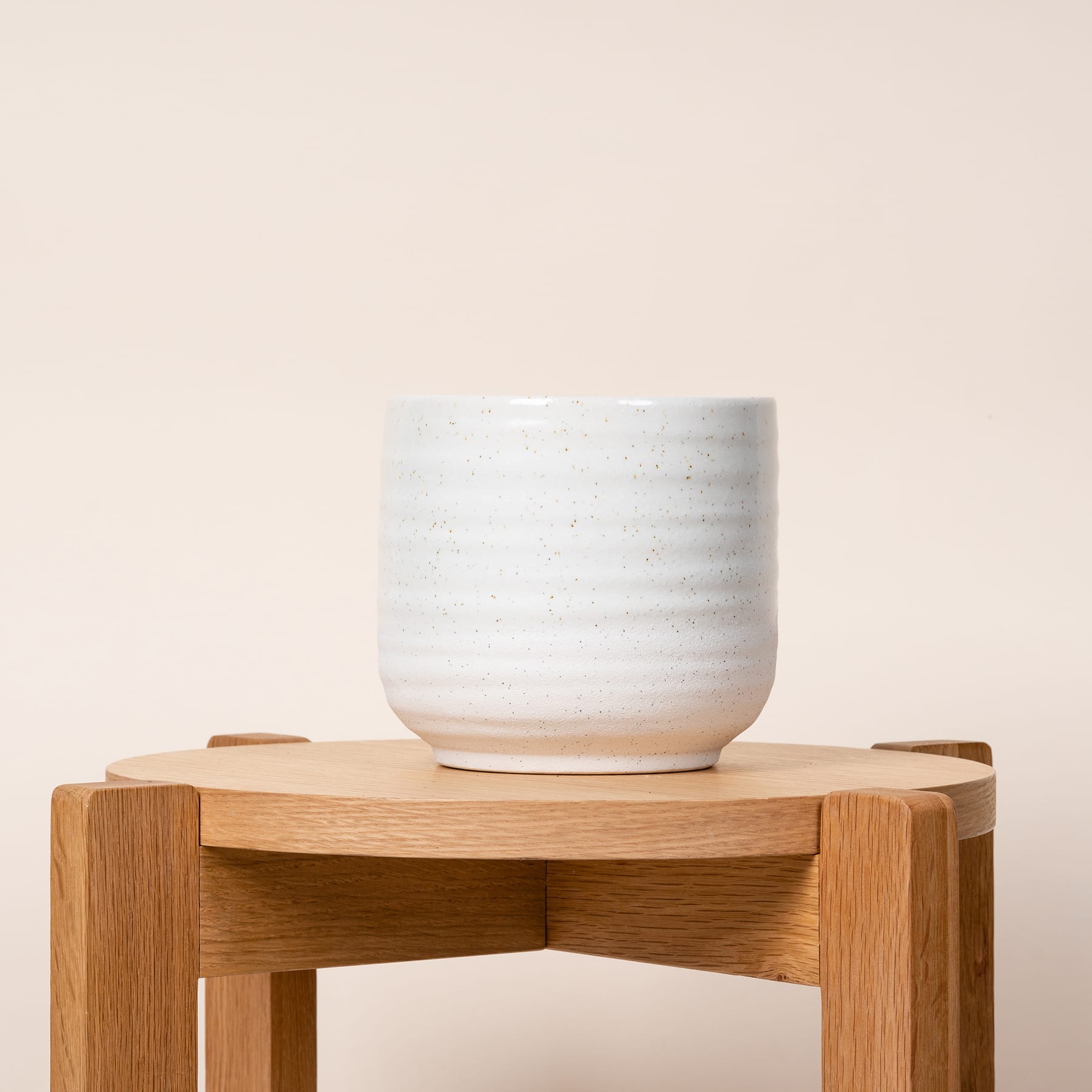 Eine weiße Keramiktasse steht auf einem Holzständer vor einem schlichten, hellen Hintergrund.