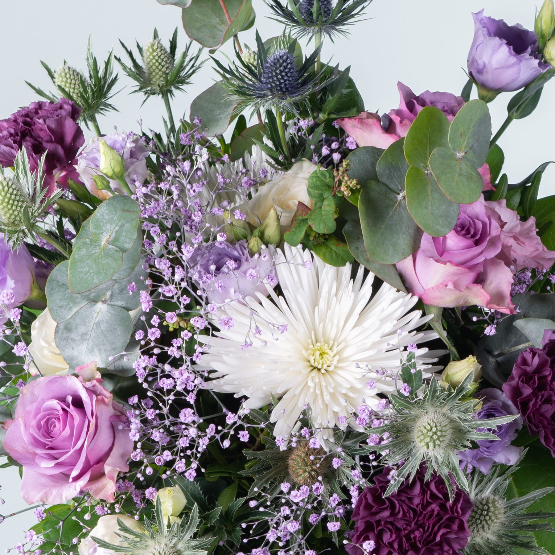 Ein lebendiger Strauß verschiedener violetter, rosa und weißer Blumen, darunter Rosen, Chrysanthemen und Disteln, arrangiert vor einem hellen Hintergrund.