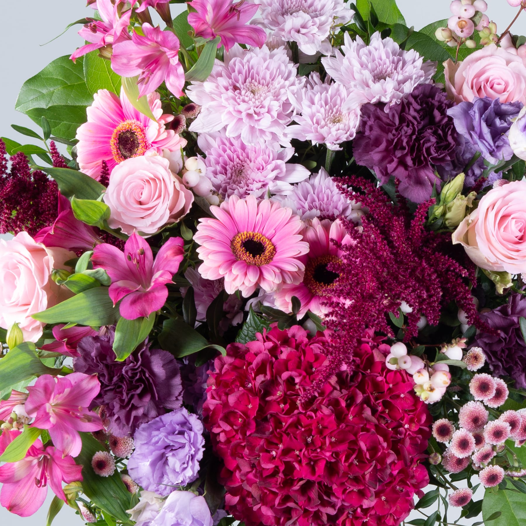 Ein lebendiger Strauß verschiedener rosa, violetter und roter Blumen, darunter Rosen, Gerbera und Chrysanthemen, vor einem hellen Hintergrund.