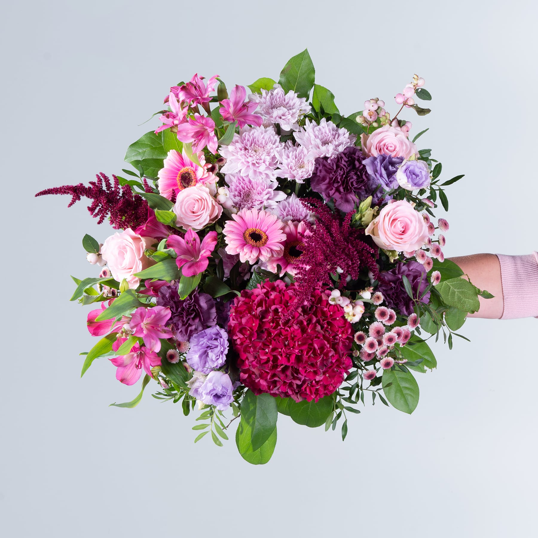 Ein lebendiger Strauß verschiedener rosa, violetter und roter Blumen, darunter Rosen, Chrysanthemen und Dahlien, üppig und farbenfroh arrangiert vor einem schlichten grauen Hintergrund.