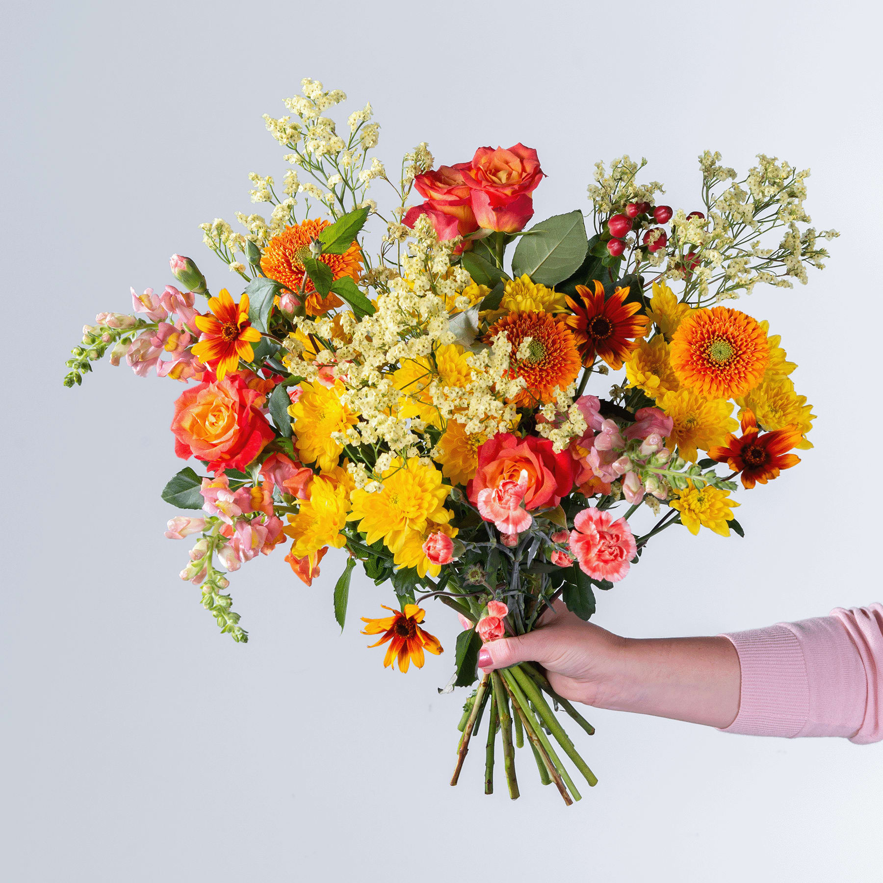 Ein leuchtender Strauß bunter Blumen, darunter Rosen, Sonnenblumen und andere Blüten, wird vor einem schlichten Hintergrund in der Hand einer Person gehalten.