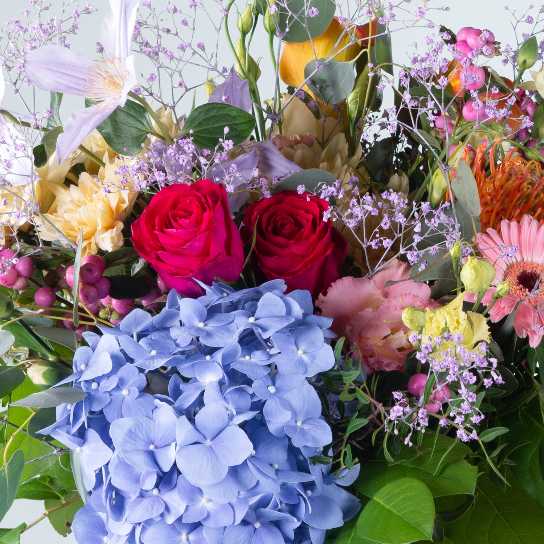 Ein farbenfroher Strauß verschiedener Blumen, darunter rote Rosen, blaue Hortensien und eine Auswahl anderer Blüten, vor einem hellen Hintergrund.