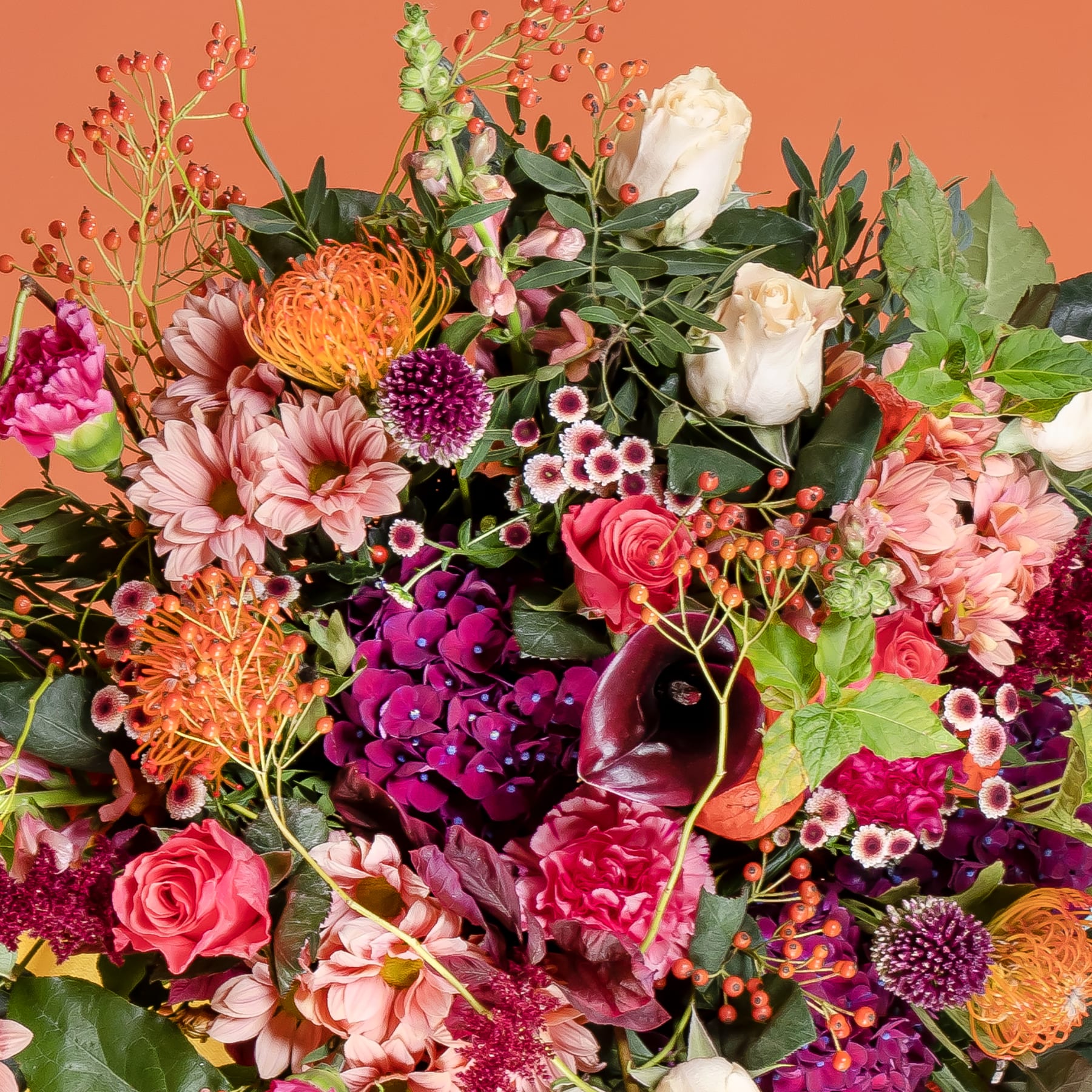 Ein lebendiger und üppiger Strauß verschiedener bunter Blumen, darunter Rosen, Dahlien, Chrysanthemen und andere Blüten, vor einem warmen orangefarbenen Hintergrund.