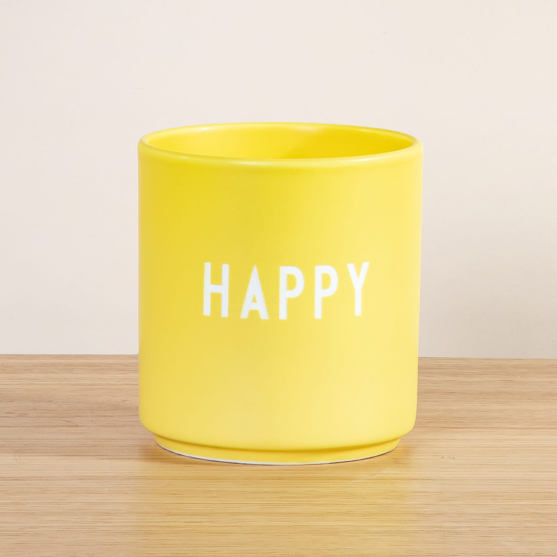 Eine leuchtend gelbe Keramiktasse mit dem Aufdruck „HAPPY“ steht auf einer Holzoberfläche.