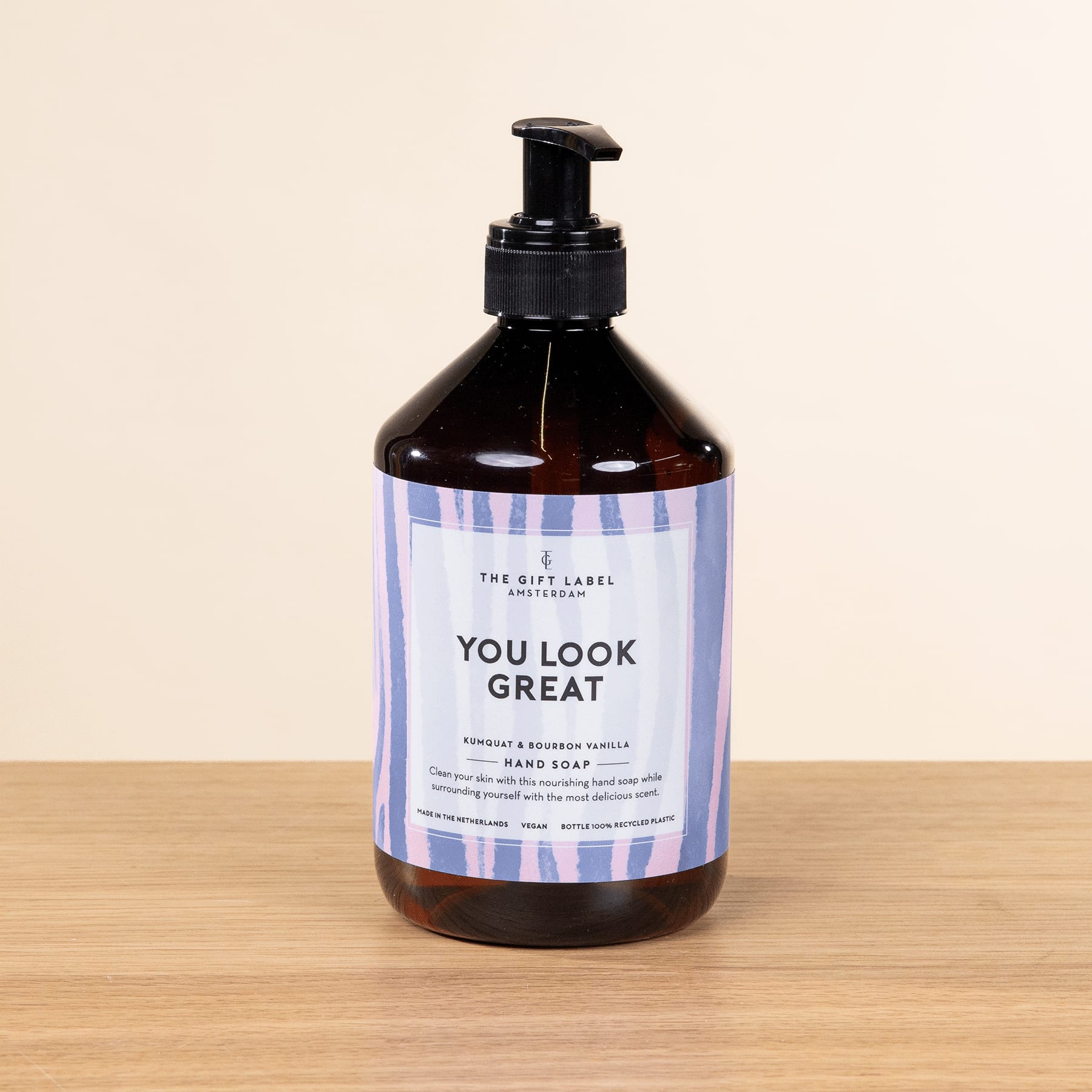 Eine schwarze Flasche mit Pumpspender und der Aufschrift „You Look Great“ steht auf einer Holzoberfläche vor einem hellen Hintergrund.