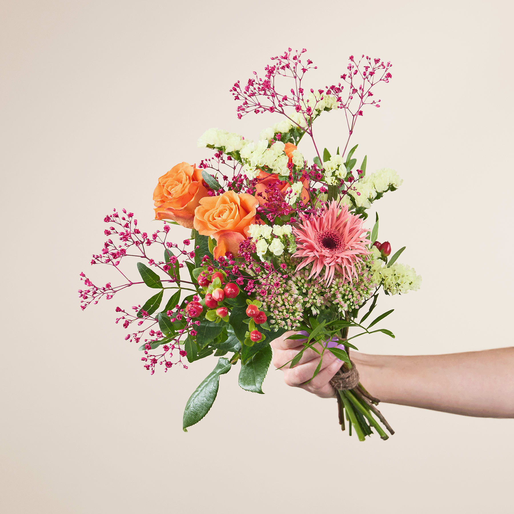 Ein leuchtender Strauß bunter Blumen, darunter orangefarbene Rosen, rosa Gerbera und verschiedene Grünpflanzen, wird vor einem schlichten Hintergrund in den Händen einer Person gehalten.