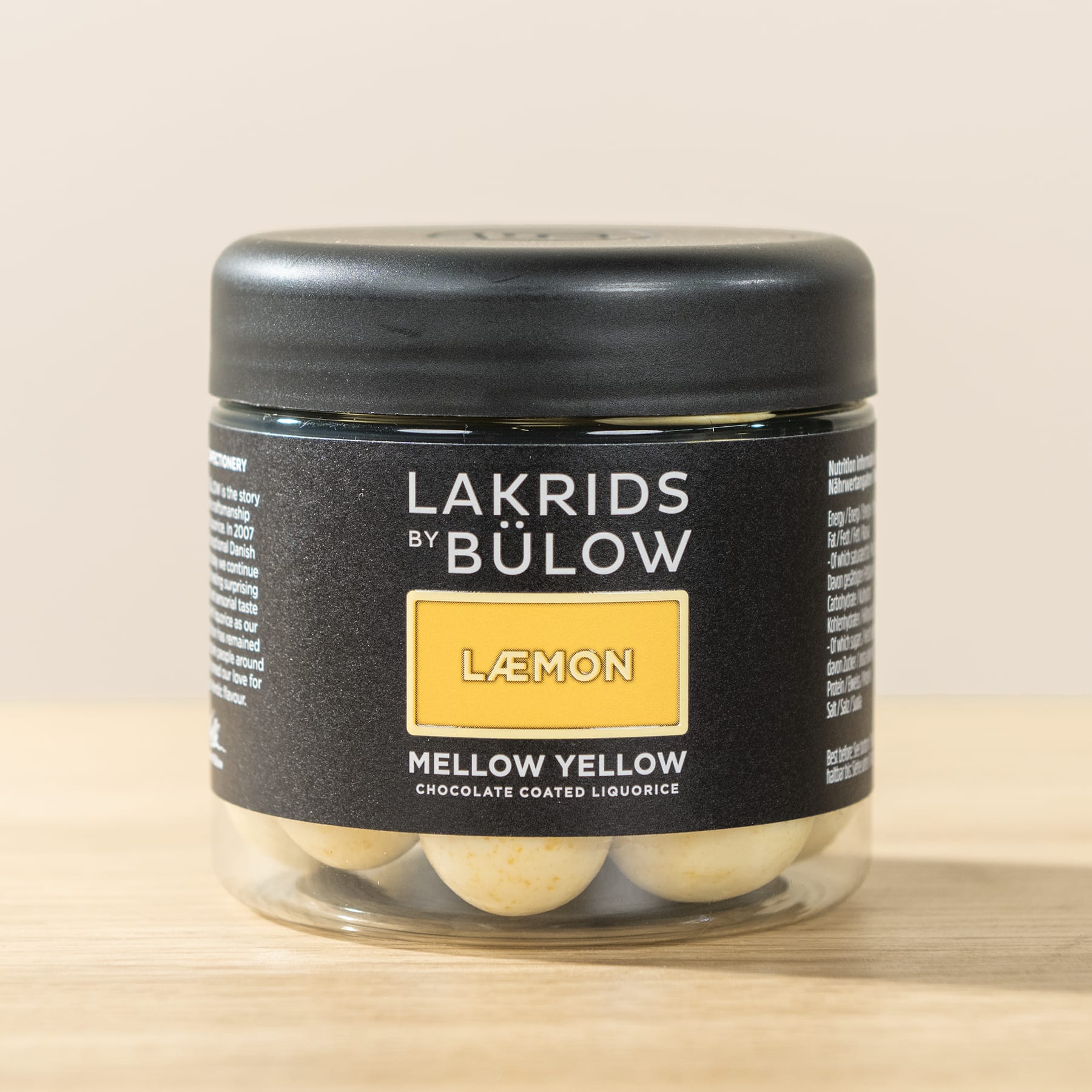 Ein schwarzes Glas mit einem gelben Etikett mit der Aufschrift „Lemon Mellow Yellow“ von Lakrids by Bulow, das auf einer hellen Oberfläche steht.