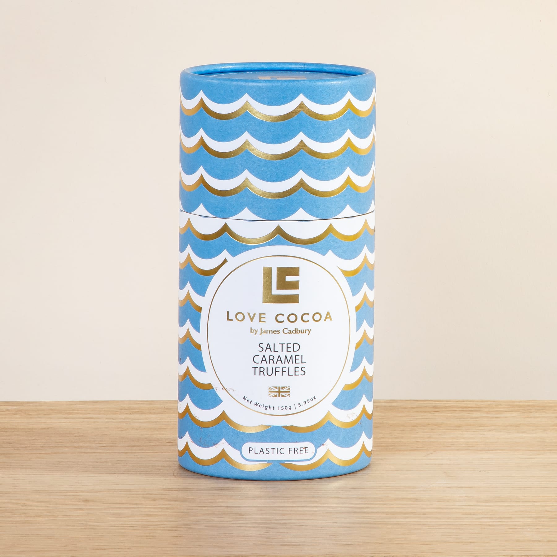 Ein zylindrischer Behälter mit einem blau-weißen Wellenmuster auf der Außenseite, mit dem „Love Cocoa“-Logo und dem Text „Salted Caramel Truffles“ auf einer Holzoberfläche.