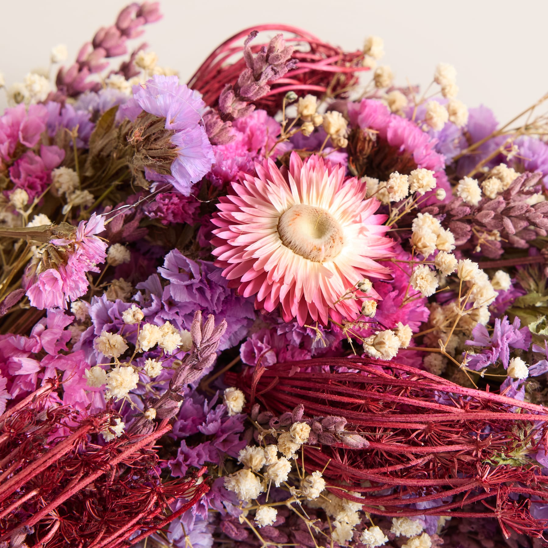 Ein leuchtender, runder Kranz aus verschiedenen violetten und weißen Blumen, darunter auch Schleierkraut, steht vor einem schlichten, hellen Hintergrund.