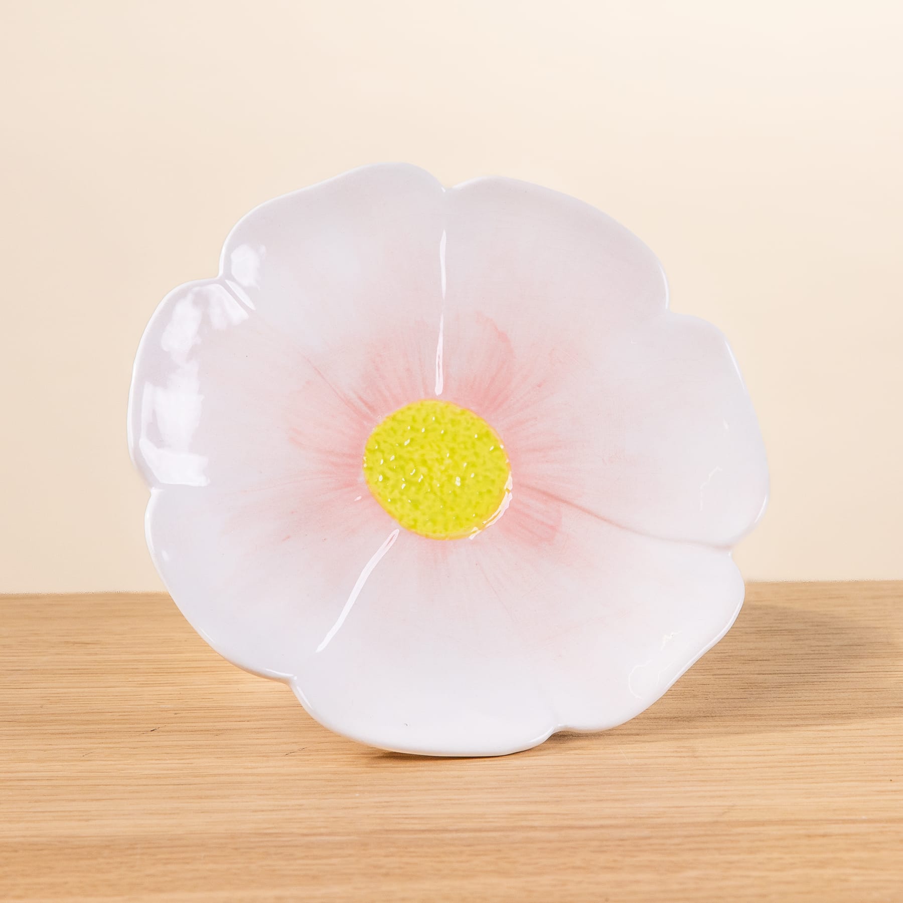 Eine große, zarte weiße Blume mit einer leuchtend gelben Mitte sitzt auf einer Holzoberfläche vor einem blassen Hintergrund.