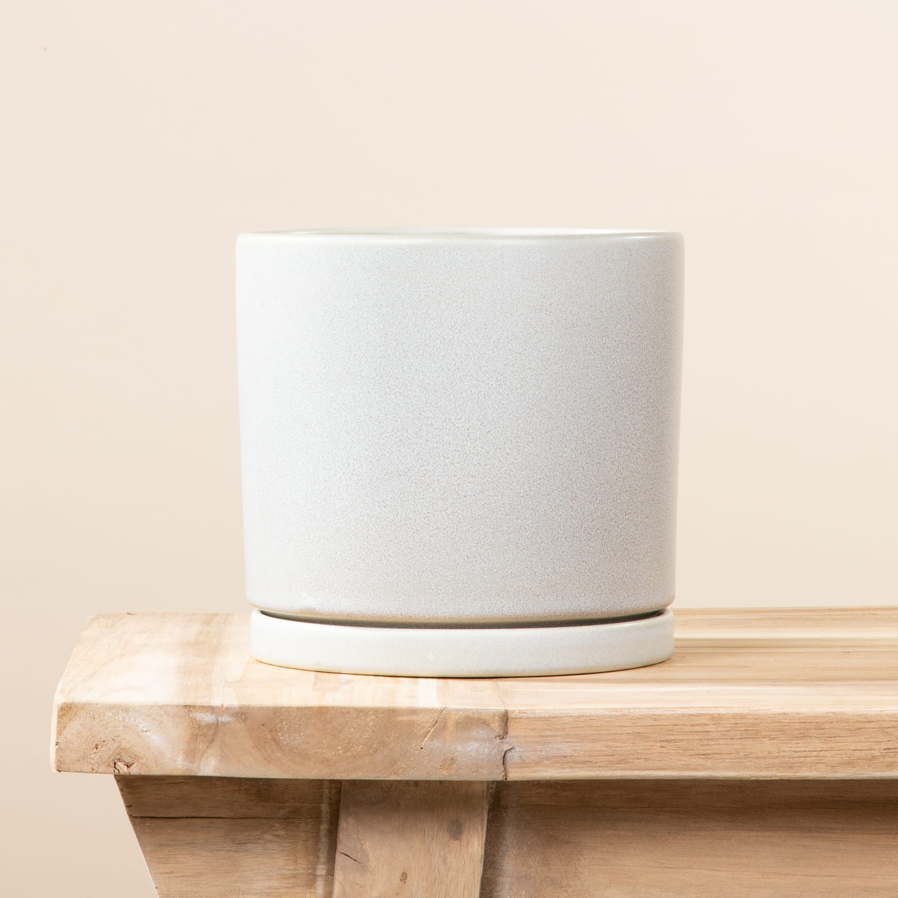 Ein weißer Blumentopf oder Topf aus Keramik steht auf einem Holzregal oder Tisch vor einem hellen Hintergrund.