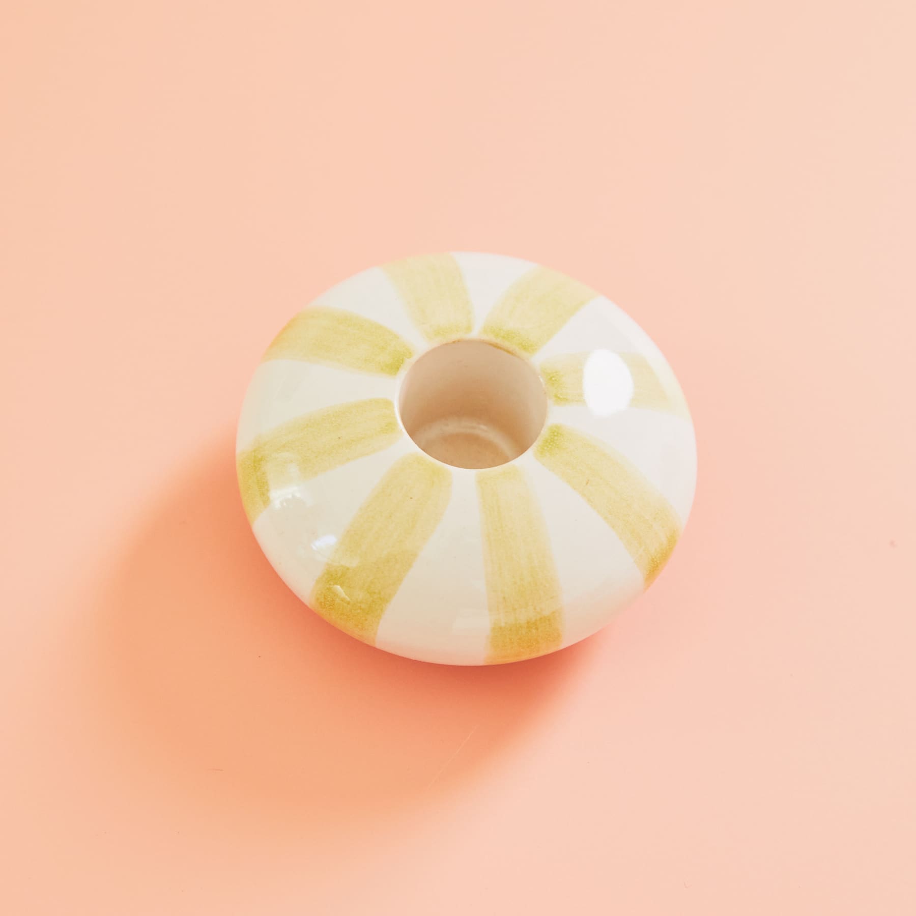 Auf einem pfirsichfarbenen Hintergrund befindet sich ein weiß-gelb gestreiftes Objekt in Donutform.