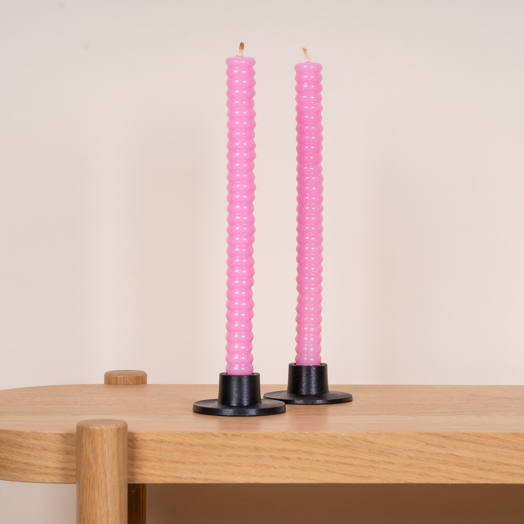 Zwei große, rosa Kerzen stehen auf einem Holztisch vor einem hellen Hintergrund.