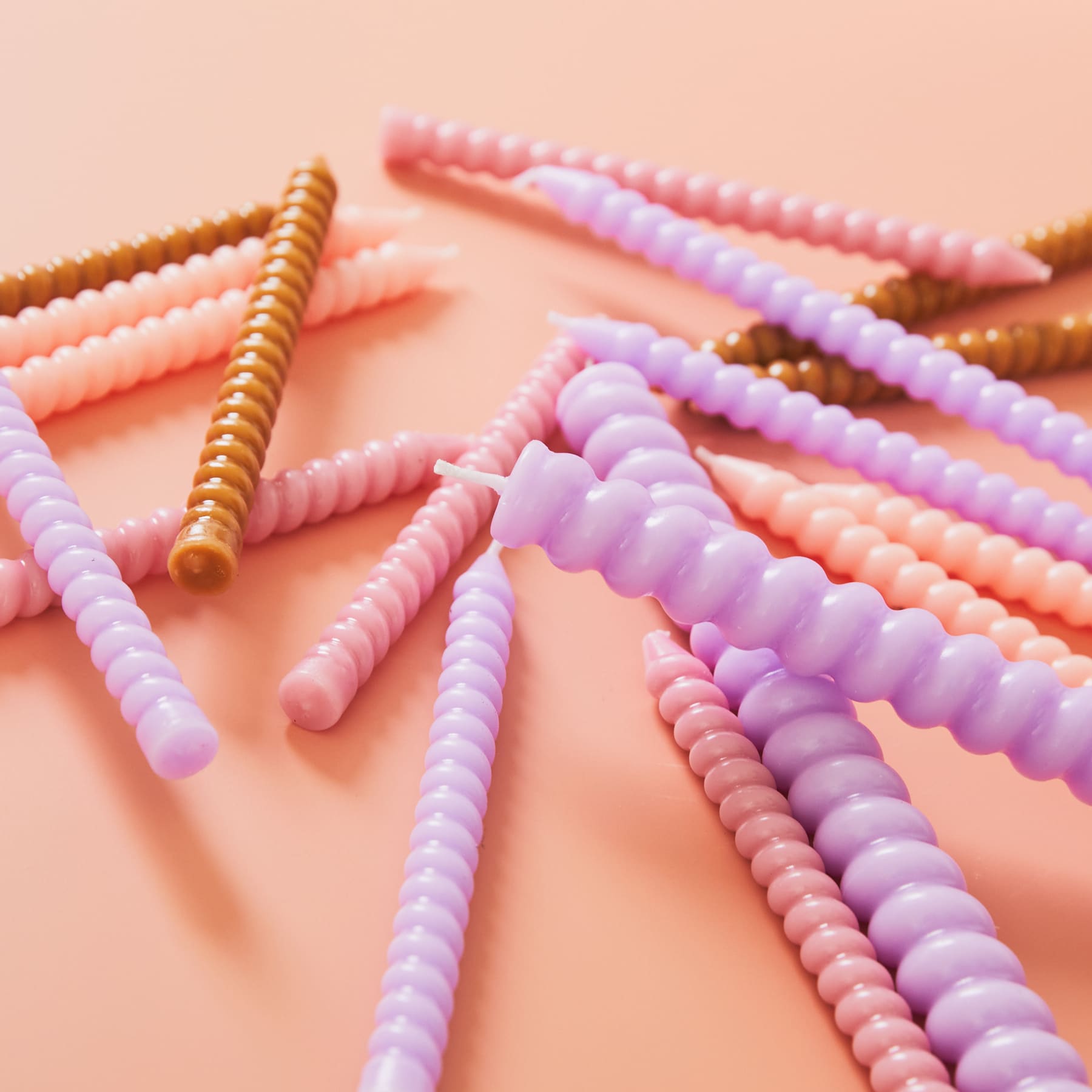 Bunte, spiralförmige Bonbons oder Konfekt in Rosa-, Lila- und Goldtönen auf pfirsichfarbenem Hintergrund.