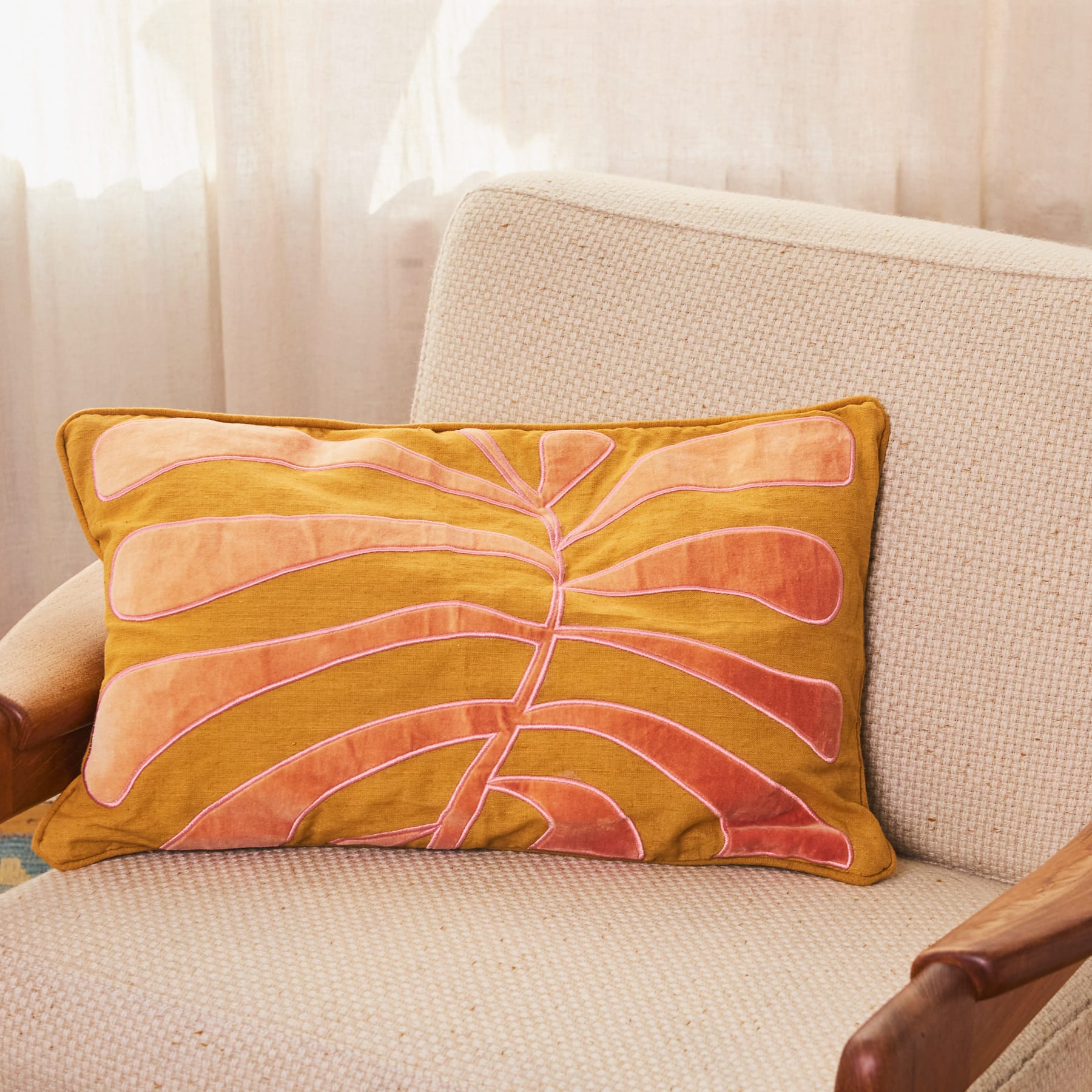 Eine gemütliche Wohnzimmereinrichtung mit einem beigen Sofa und einem dekorativen Sofakissen mit einem lebendigen, abstrakten, blattähnlichen Muster in Gelb- und Orangetönen.