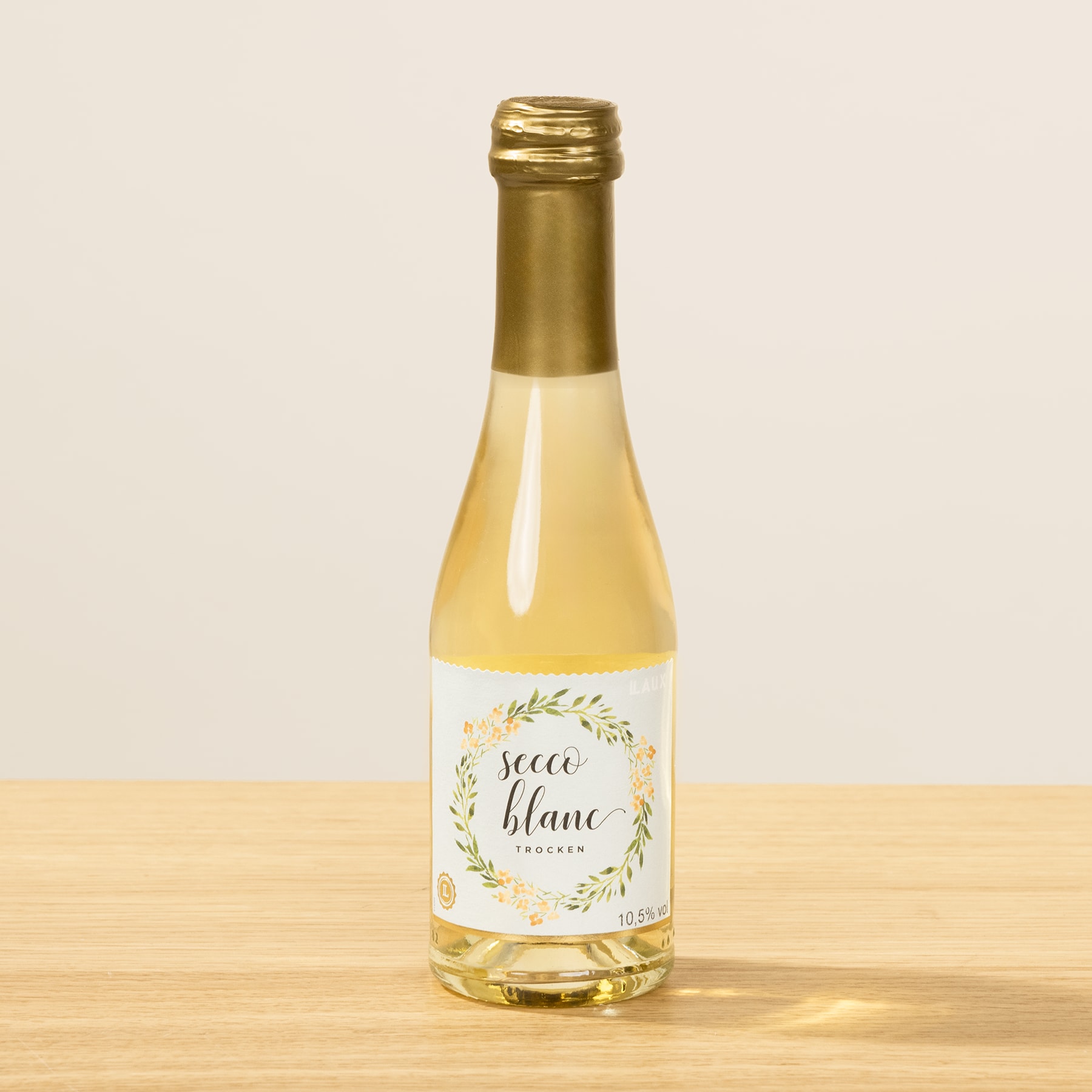 Eine Glasflasche Weißwein mit goldenem Verschluss steht auf einer Holzoberfläche vor einem schlichten Hintergrund.
