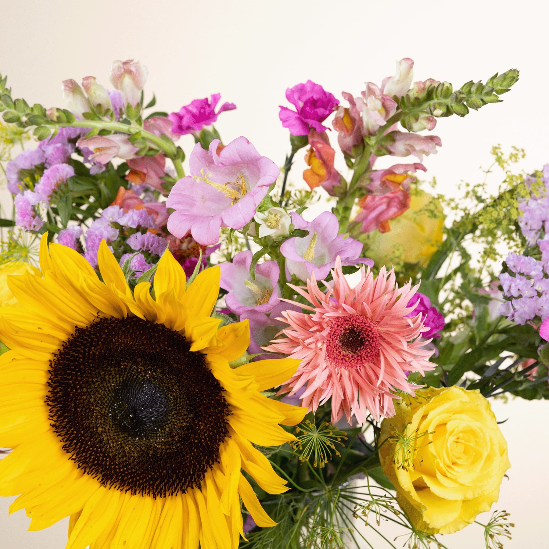 Ein lebendiger Strauß bunter Blumen, darunter eine Sonnenblume, rosa Gerbera und verschiedene andere Blüten, vor einem schlichten Hintergrund.
