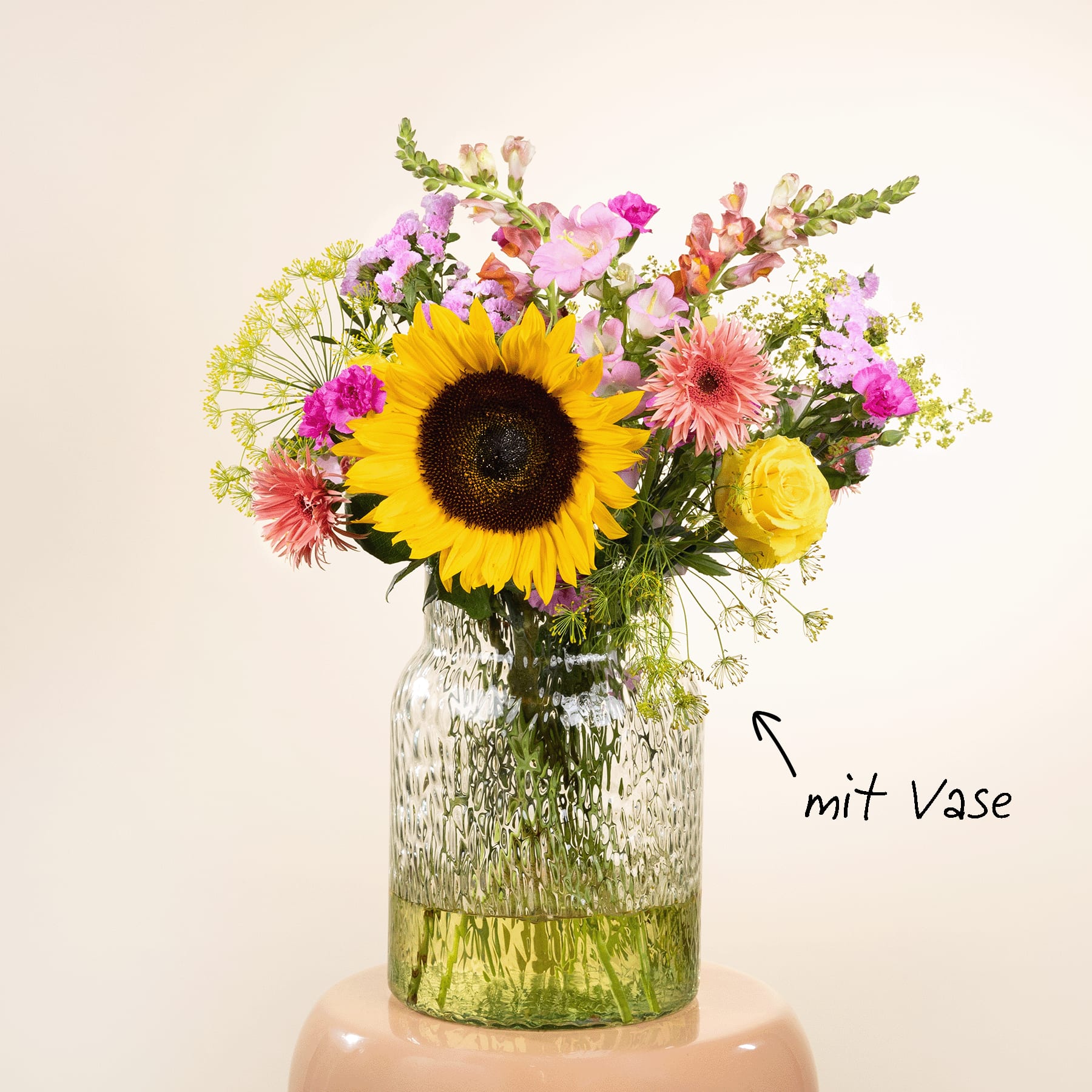 Ein lebendiger Strauß aus Sonnenblumen, Gänseblümchen und anderen bunten Blumen, arrangiert in einer Glasvase mit strukturierter Oberfläche, vor einem schlichten, hellen Hintergrund.