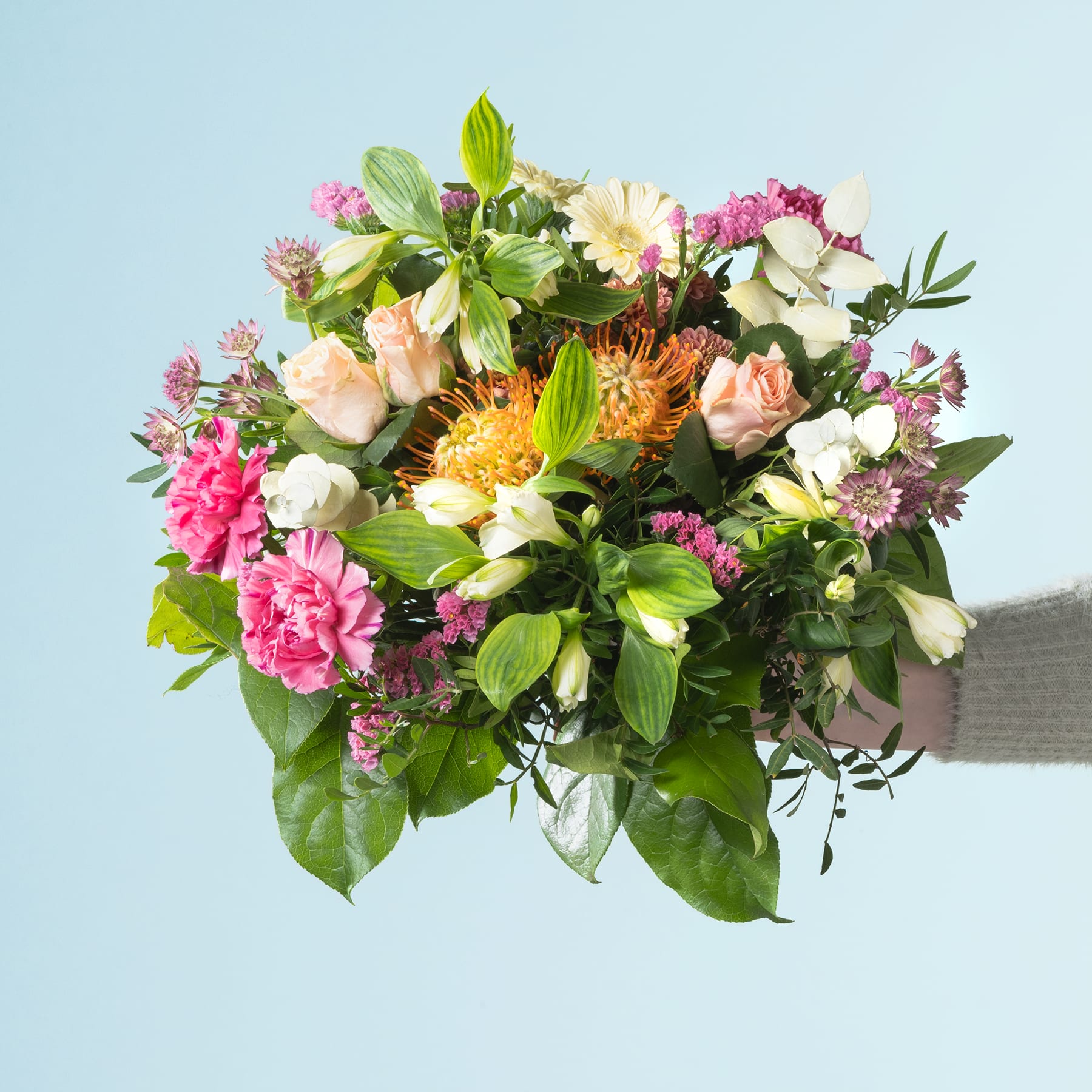 Ein lebendiger Strauß verschiedener bunter Blumen, darunter Rosen, Gänseblümchen und andere Blüten, arrangiert in einer Vase vor einem schlichten blauen Hintergrund.