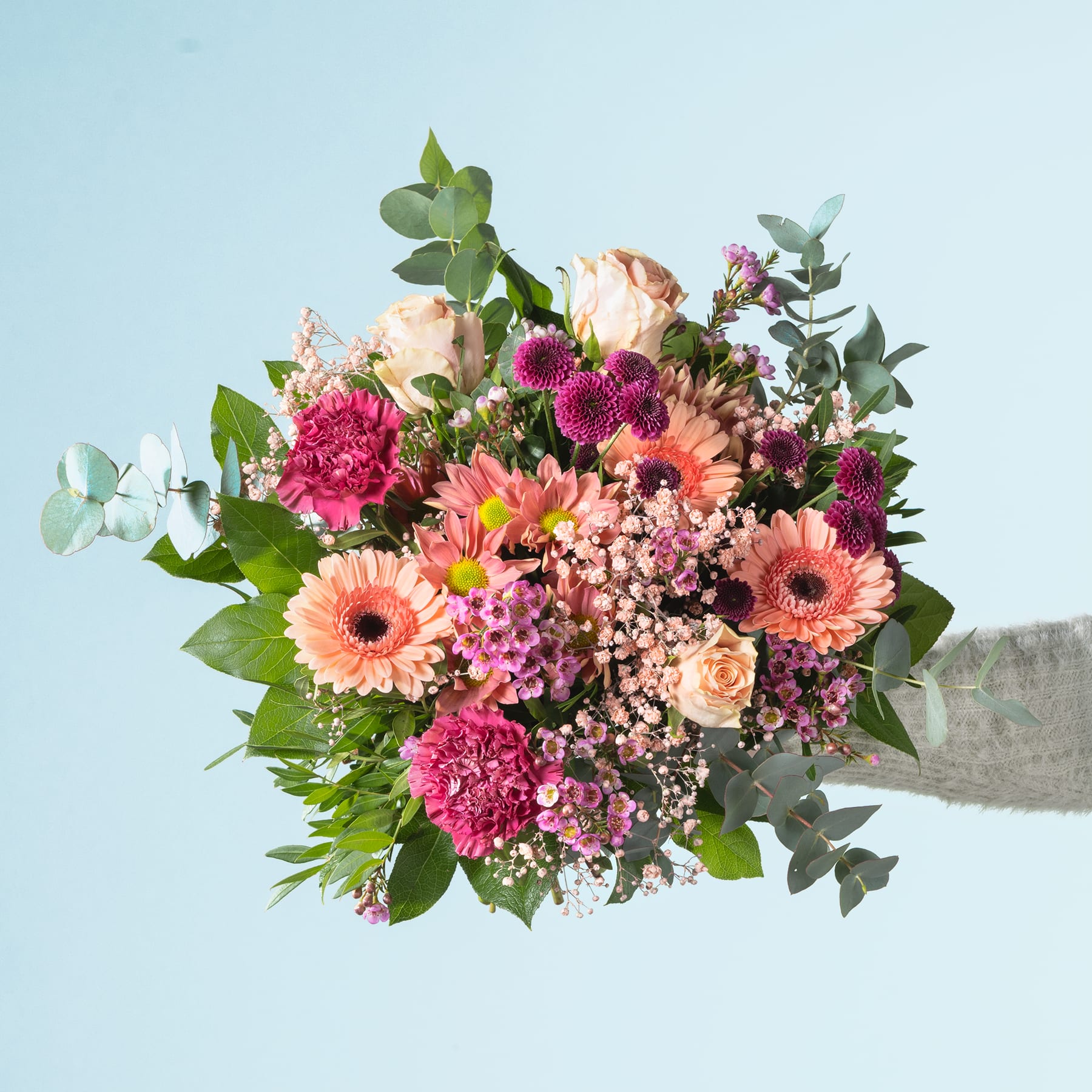 Ein lebendiger Strauß verschiedener bunter Blumen, darunter Gerbera, Rosen und Nelken, vor einem sanften blauen Hintergrund.