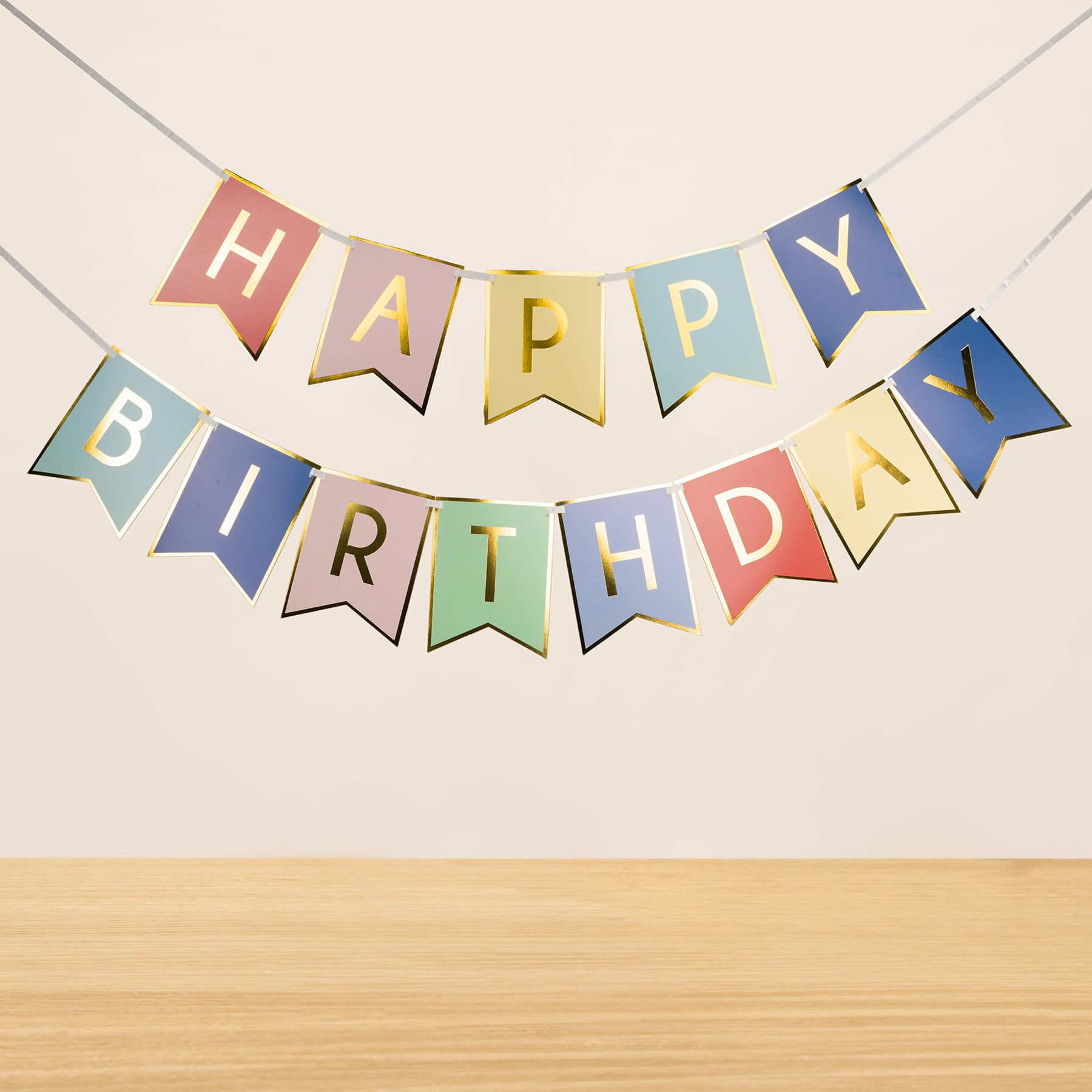 Vor einem schlichten Hintergrund hängt ein buntes „Happy Birthday“-Banner, der Text ist auf verschiedenfarbigen Fahnen zu sehen.