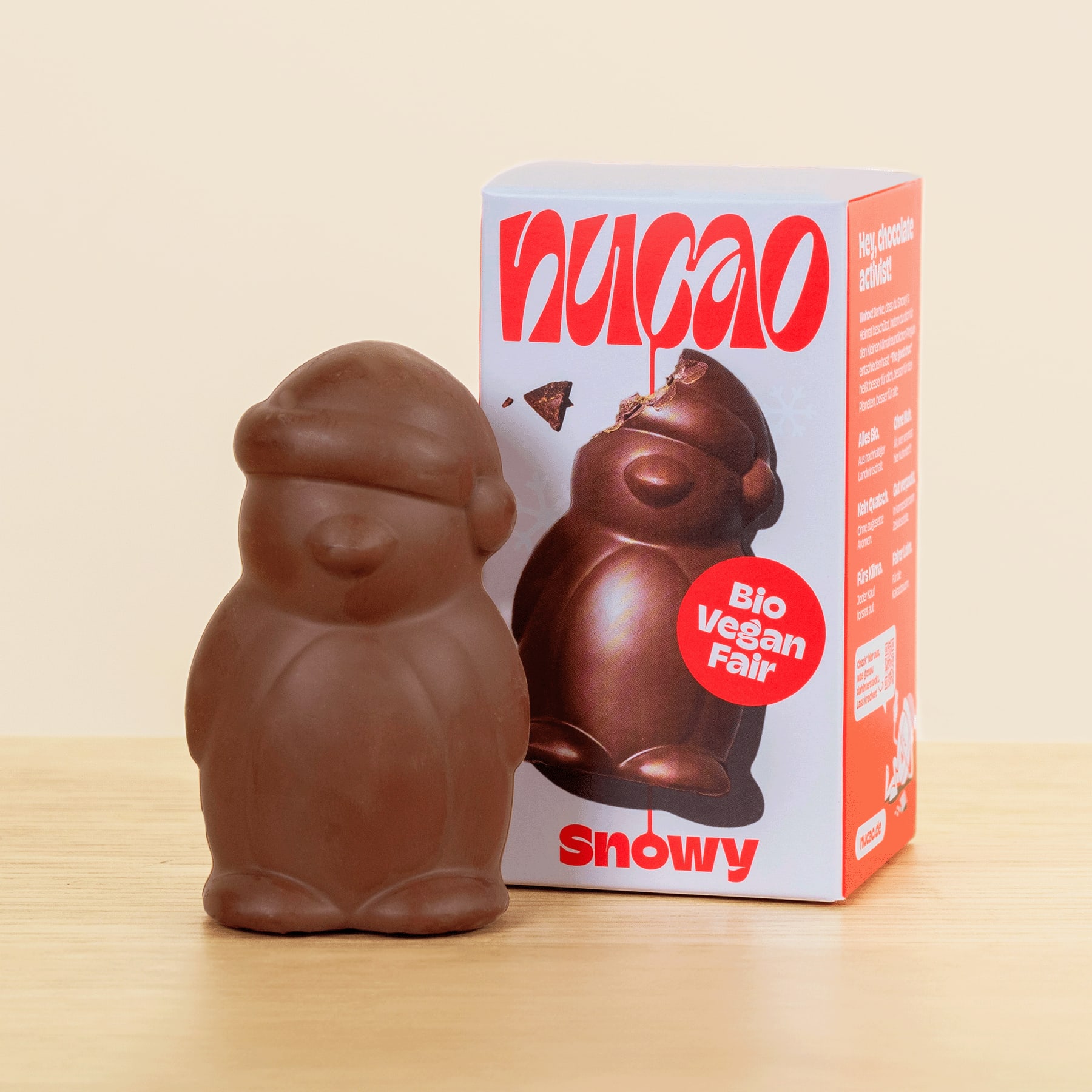 Eine Schokoladenfigur einer Figur, die einem Schneemann oder einer ähnlichen Figur ähnelt, neben einer Schachtel mit der Aufschrift „Vegan Fair“ und „Snowy“.