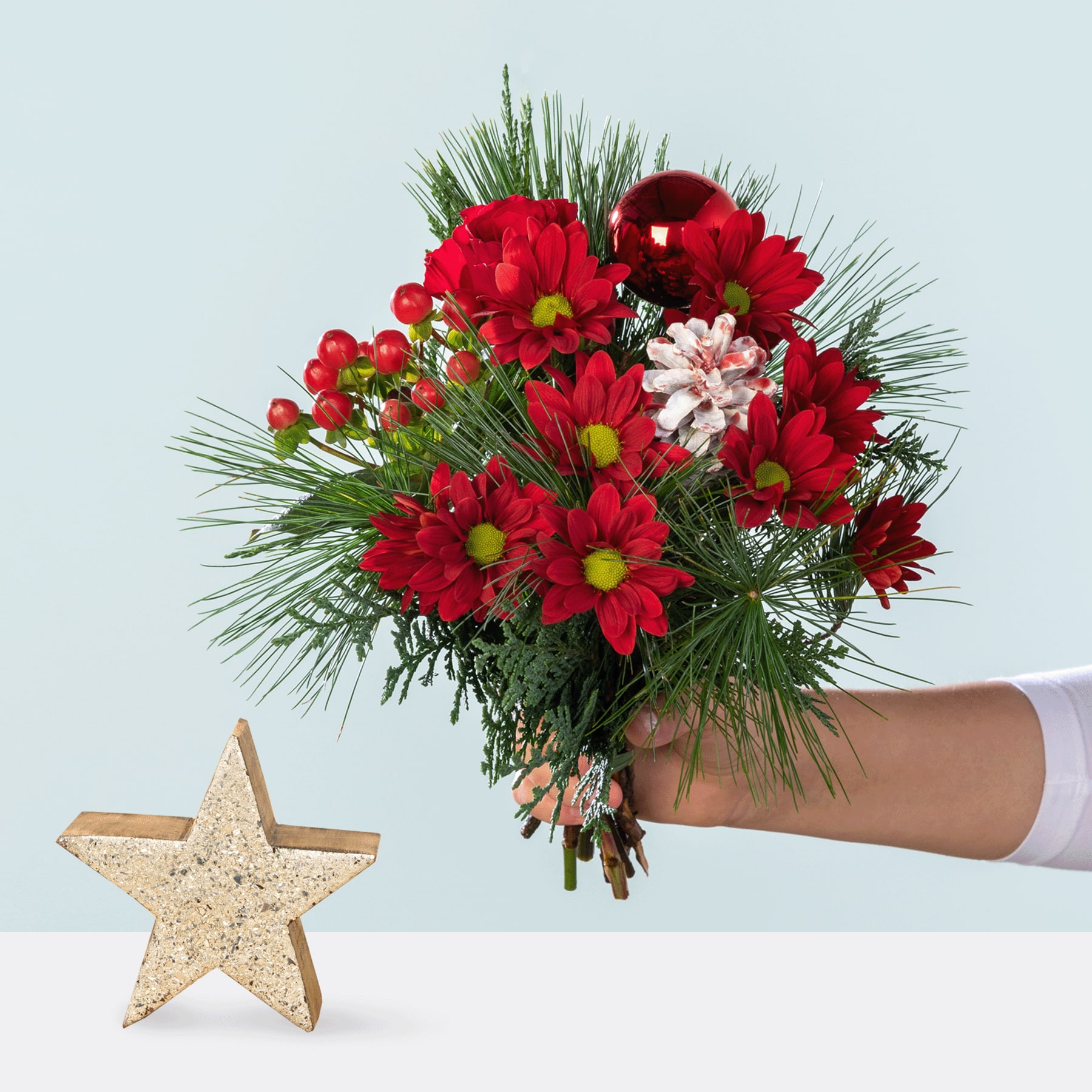 Ein leuchtender Strauß roter und rosa Blumen, darunter Gänseblümchen und Pfingstrosen, wird vor einem schlichten Hintergrund in der Hand gehalten, im Vordergrund ist ein glitzernder goldener Stern zu sehen.
