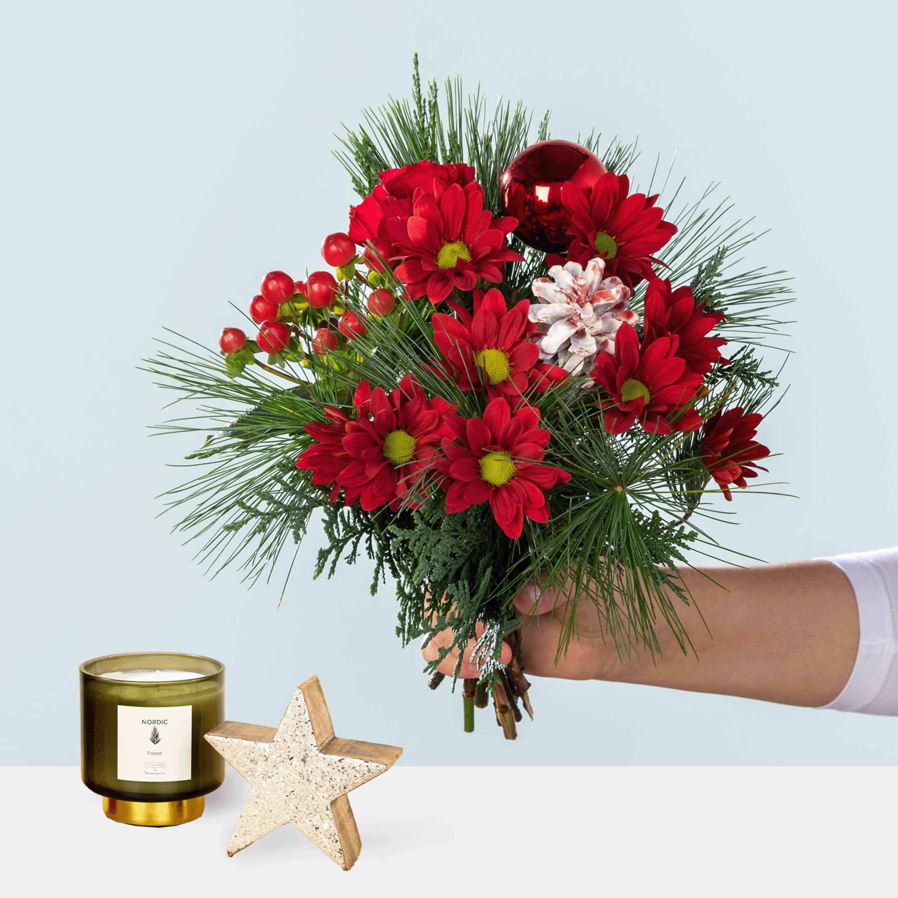 Ein leuchtender Strauß roter und rosa Blumen, darunter Chrysanthemen und Pfingstrosen, in der Hand gehalten vor einem schlichten Hintergrund, begleitet von einer Kerze und einem Seestern.