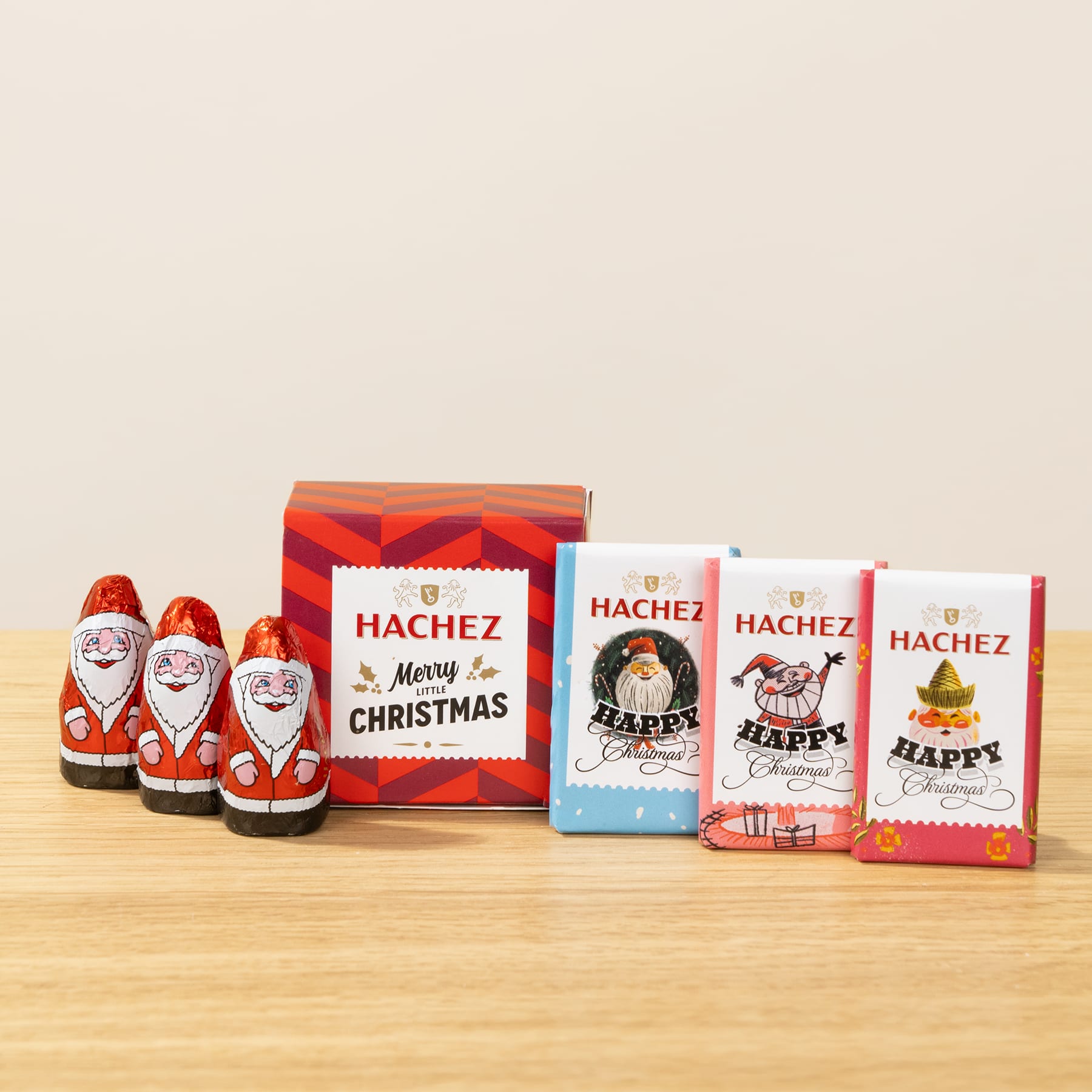 Das Bild zeigt verschiedene Schokoladenprodukte mit Weihnachtsmotiven, darunter Weihnachtsmannfiguren und Pralinenschachteln, die auf einer Holzoberfläche vor einem schlichten Hintergrund angeordnet sind.